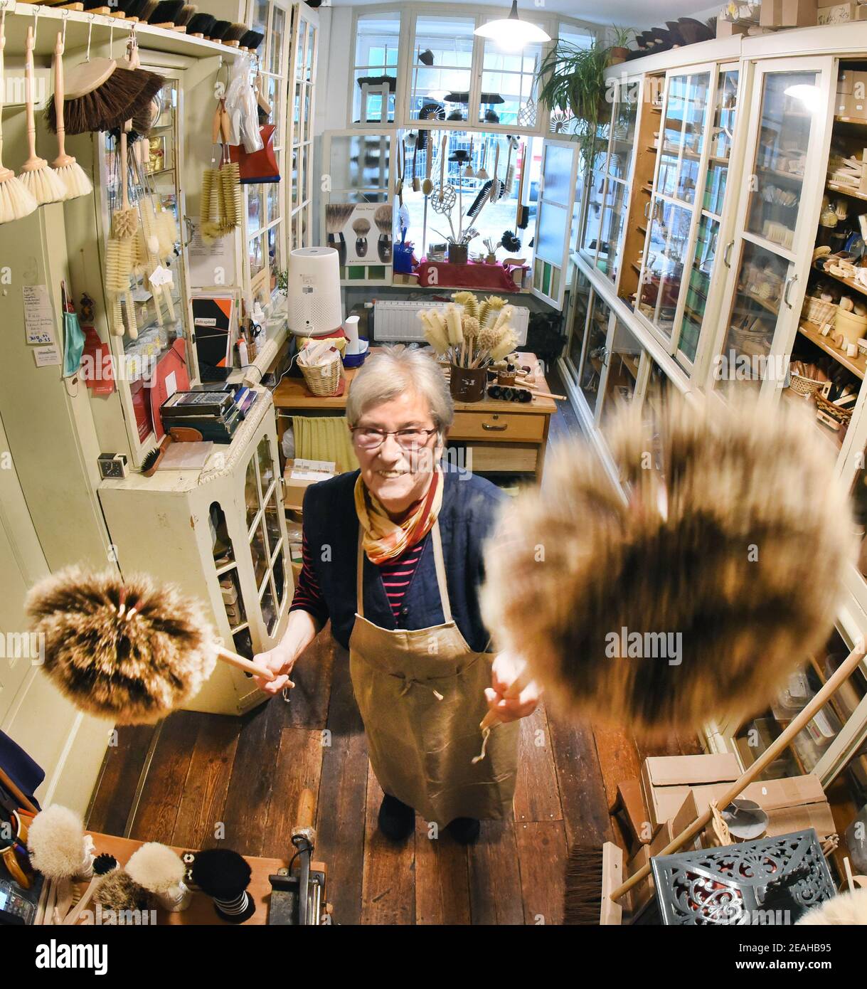 08. Februar 2021, Sachsen-Anhalt, Naumburg: In ihrer kleinen Bürstenmanufaktur, die auch als Verkaufsraum dient, hält die 81-jährige Bürstenmanufaktur Ursula Römer zwei Federstauber in den Händen. Obwohl ihr Laden wegen der Pandemie geschlossen ist, kommen derzeit viele Bestellungen aus ganz Deutschland per Telefon oder schriftlich für große und kleine Besen, Spinnenfeger, Federstauber oder sogar Wand- und Deckenbesen. In ihrem traditionellen Laden, den ihr Urgroßvater 1885 eröffnete, stellt die 81-Jährige ihre Pinsel und Besen mit einer Vielzahl von Borsten auf alte, traditionelle Weise mit der Hand her Stockfoto