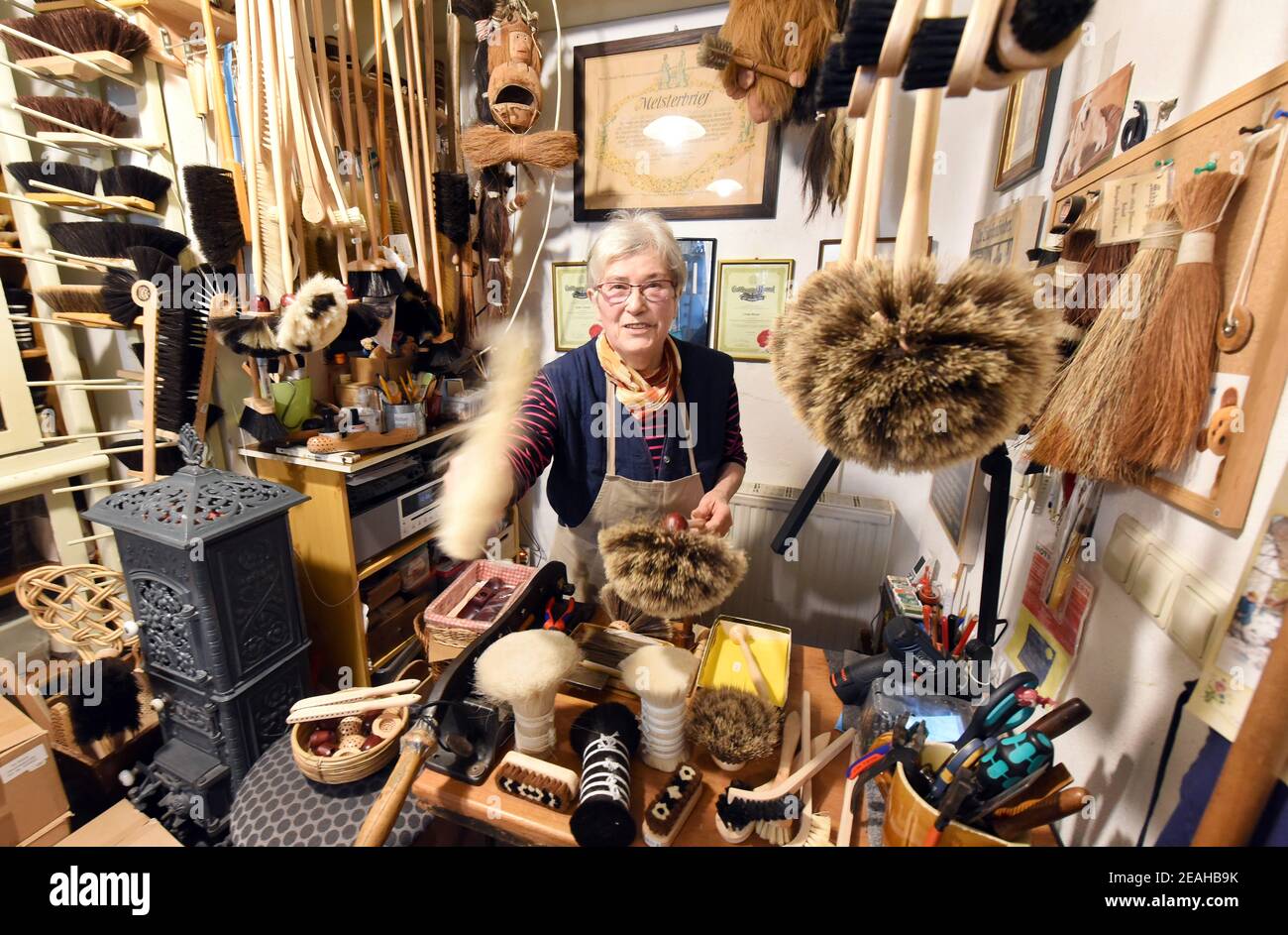 08. Februar 2021, Sachsen-Anhalt, Naumburg: In ihrer kleinen Bürstenmanufaktur, die auch als Verkaufsraum dient, arbeitet die 81-jährige Bürstenmanufaktur Ursula Römer an Federstauben. Obwohl ihr Laden wegen der Pandemie geschlossen ist, kommen derzeit viele Bestellungen aus ganz Deutschland per Telefon oder schriftlich für große und kleine Besen, Spinnenfeger, Federstauber oder sogar Wand- und Deckenbesen. In ihrem traditionellen Laden, den ihr Urgroßvater 1885 eröffnete, stellt die 81-Jährige ihre Bürsten und Besen mit einer Vielzahl von Borsten auf alte, traditionelle Weise mit dem handziehenden Metho her Stockfoto