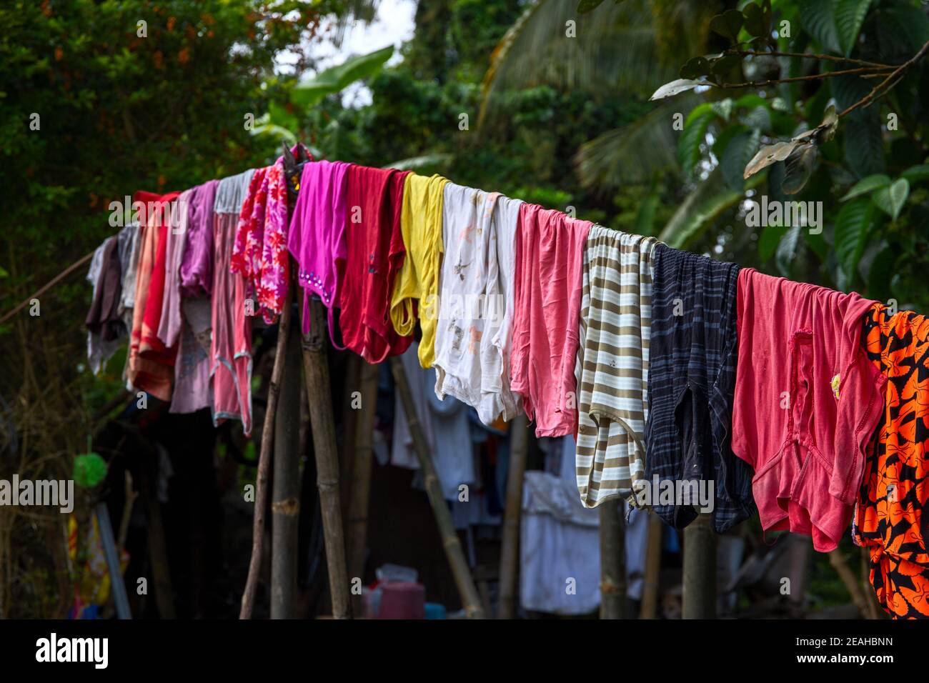 Bunte Kleidung hängt am Seil im grünen Garten. Mehrfarbige Textilbekleidung im asiatischen Dorf. Rustikale Lifestyle Hygiene auf dem Land. Social-Media-Eissu Stockfoto
