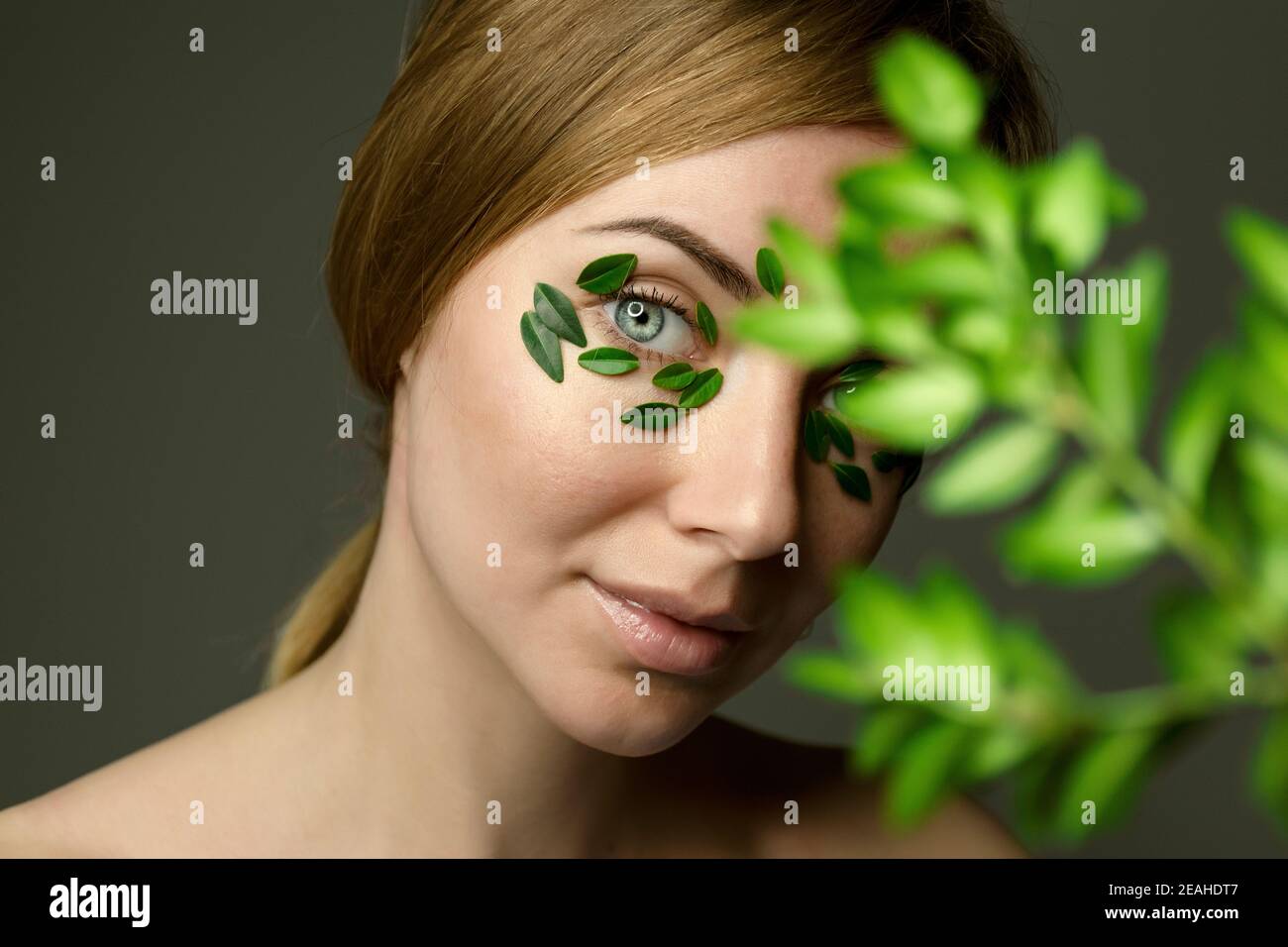 Porträt einer jungen Frau mit natürlichen Make-up verschwommen mit unscharf Buchsbaum Zweig. Grüne Blätter Flecken auf Gesicht. Konzept der Kräutermedizin. Stockfoto