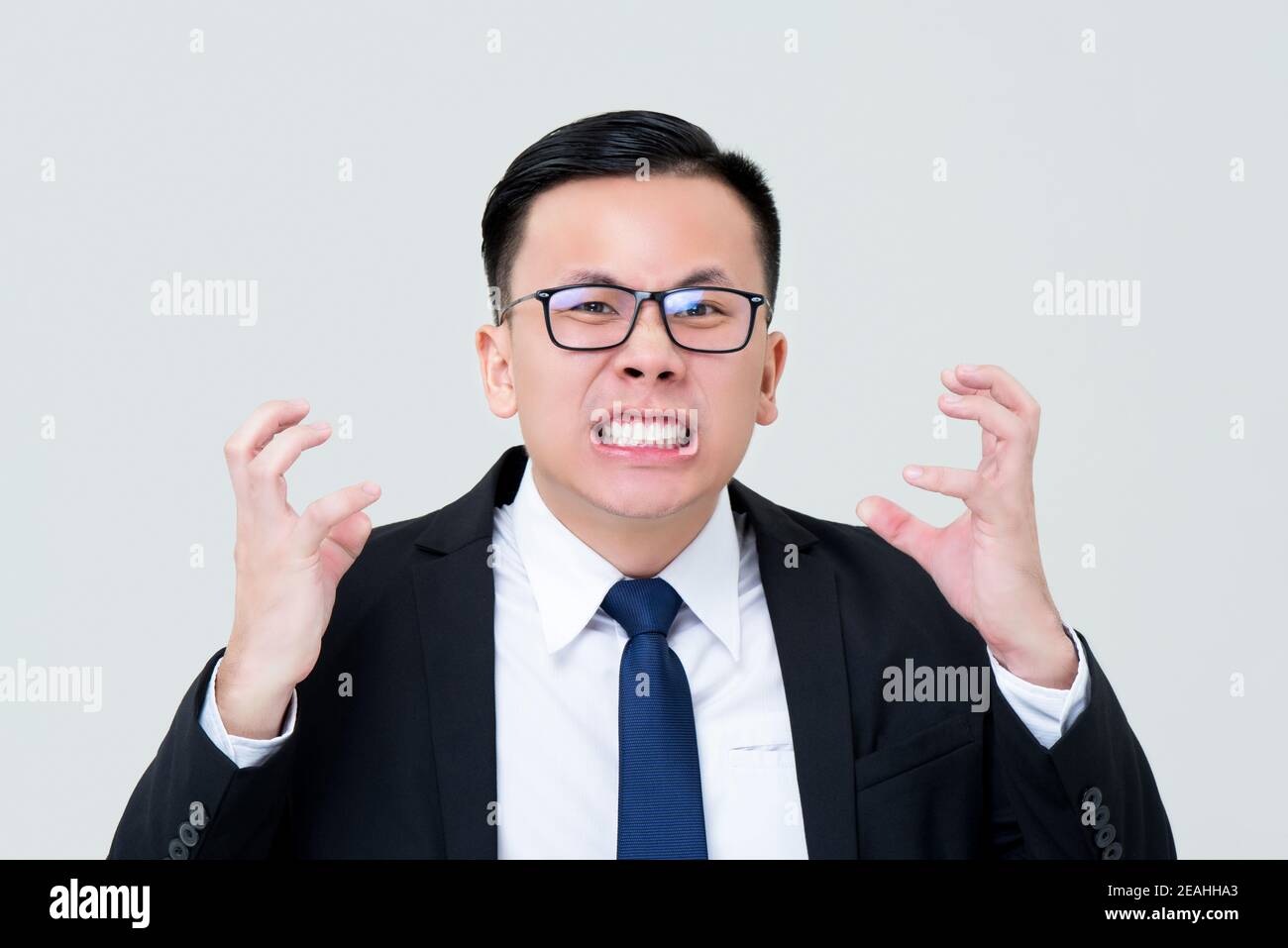 Grinsend asiatischen Geschäftsmann Gefühl wütend mit Händen quetschen isoliert auf Grauer Hintergrund Stockfoto