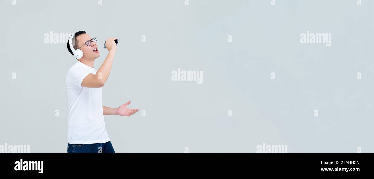 Junger asiatischer Mann mit Kopfhörern, der Musik vom Handy hört Telefon und Gesang isoliert auf hellgrauem Banner Hintergrund mit Speicherplatz kopieren Stockfoto