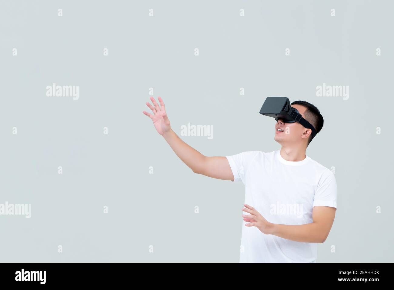 Aufgeregter Mann, der Hand ausstreut, während er 3D Simulationsvideo ansieht Von Virtual Reality oder VR-Brille auf hellgrauem Hintergrund Stockfoto