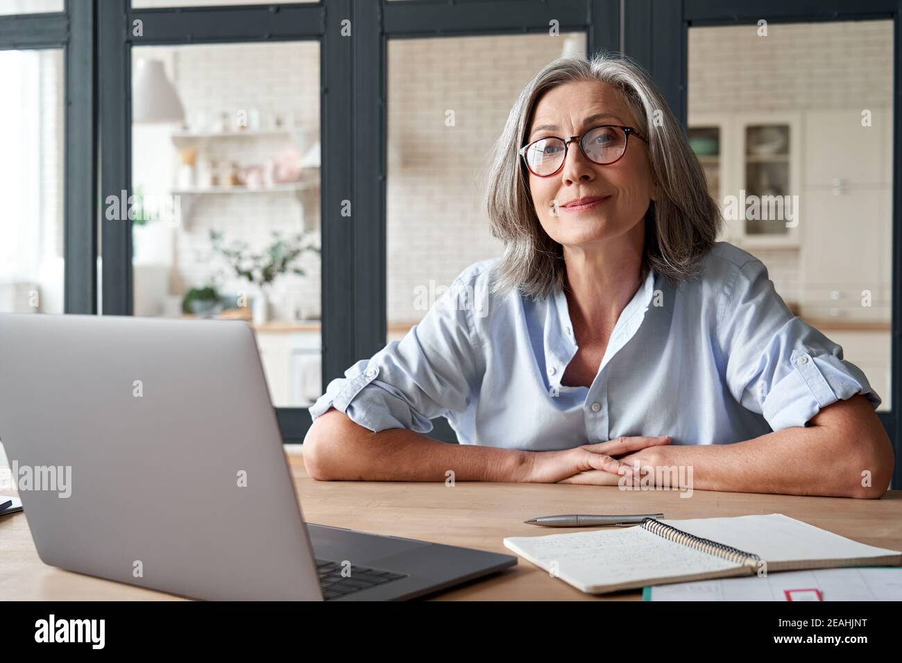 Lächelnd reife Frau mittleren Alters sitzt am Arbeitsplatz mit Laptop, Porträt. Stockfoto