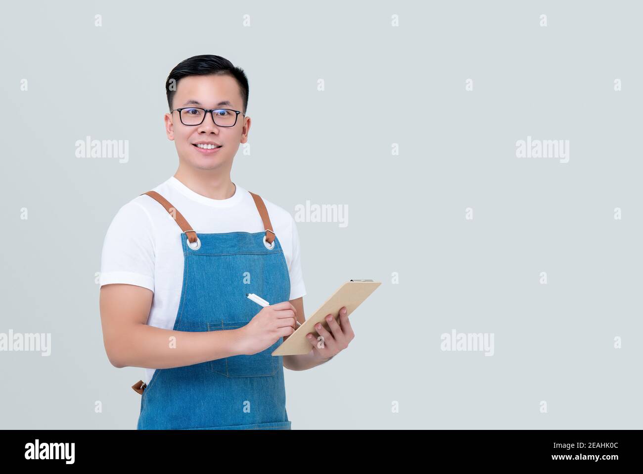 Junger asiatischer Mann Startup-Geschäft Inhaber trägt Schürze, die Ordnung nimmt Auf Zwischenablage und Blick auf Kamera isoliert auf hellgrau Hintergrund Stockfoto