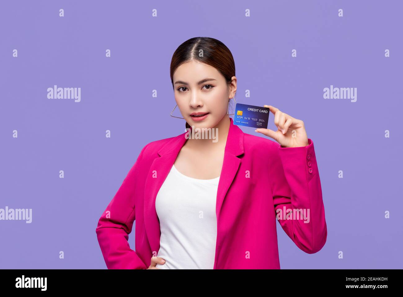 Schöne asiatische Frau in bunten rosa Anzug zeigt Kreditkarte In der Hand für Finanz- und bargeldlose Gesellschaftskonzepte Stockfoto