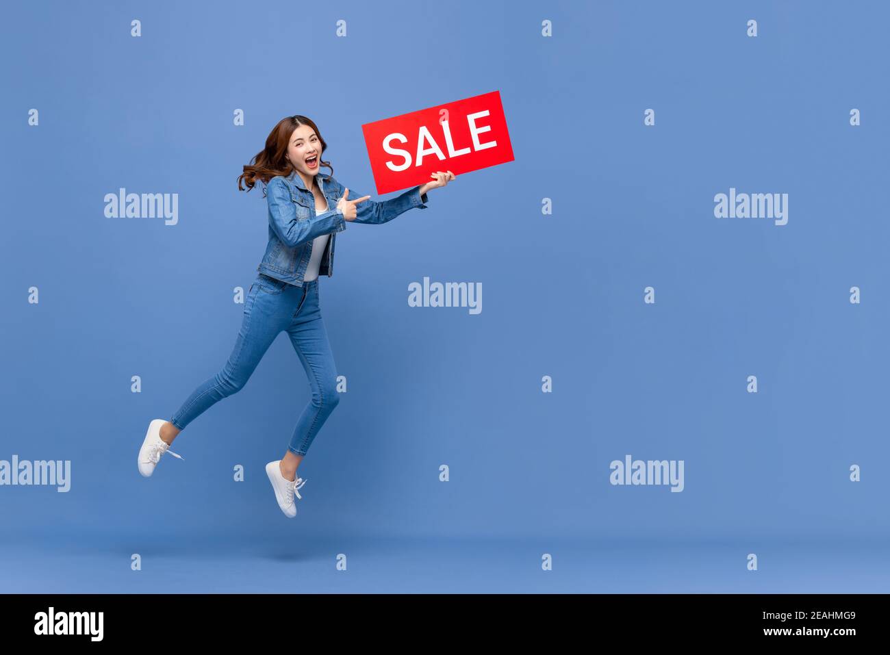 Aufgeregt asiatische Frau in Casual jean Kleidung springen mit rot Verkauf Zeichen in der Hand isoliert auf hellblauem Hintergrund mit Speicherplatz kopieren Stockfoto