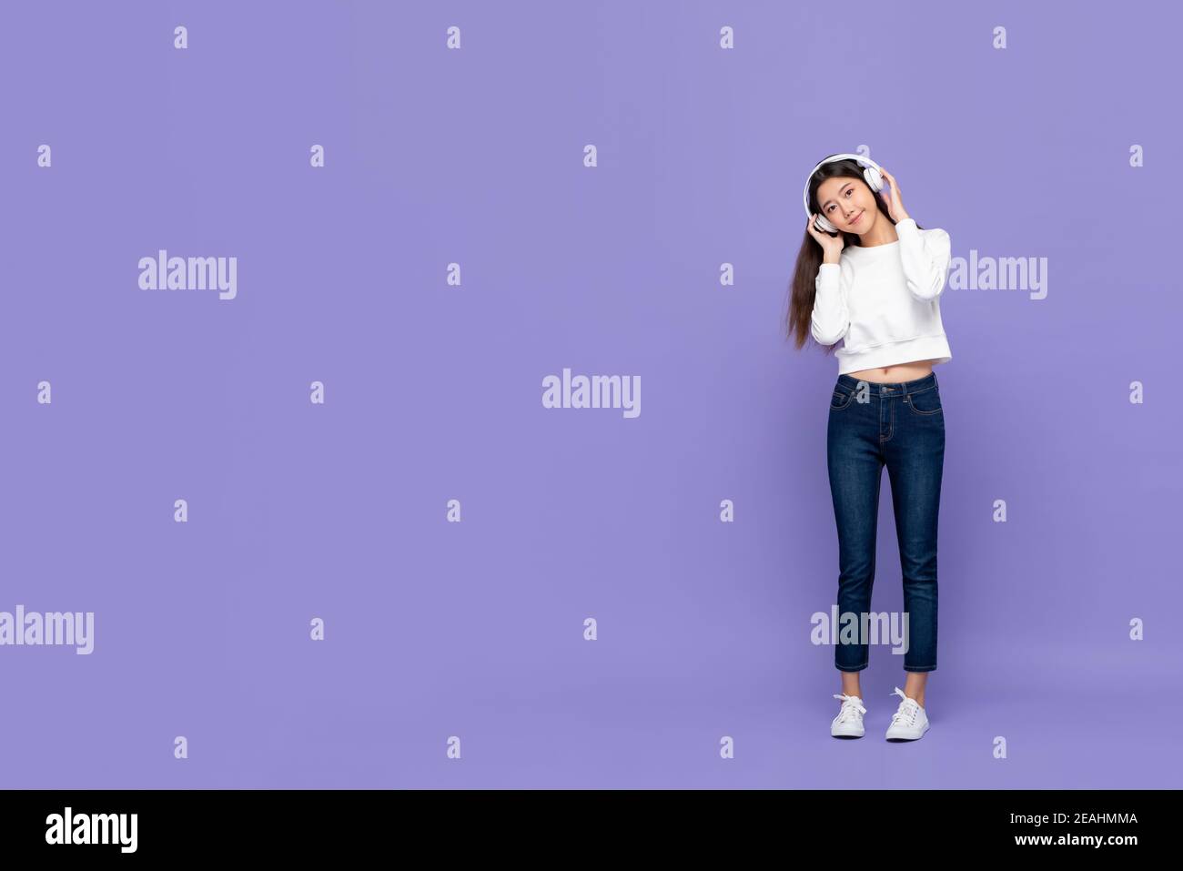 Junge hübsche nette asiatische Frau lächelnd berühren Kopfhörer und lehnte Kopf, während Sie Musik auf violettem Hintergrund mit isoliert hören Speicherplatz kopieren Stockfoto