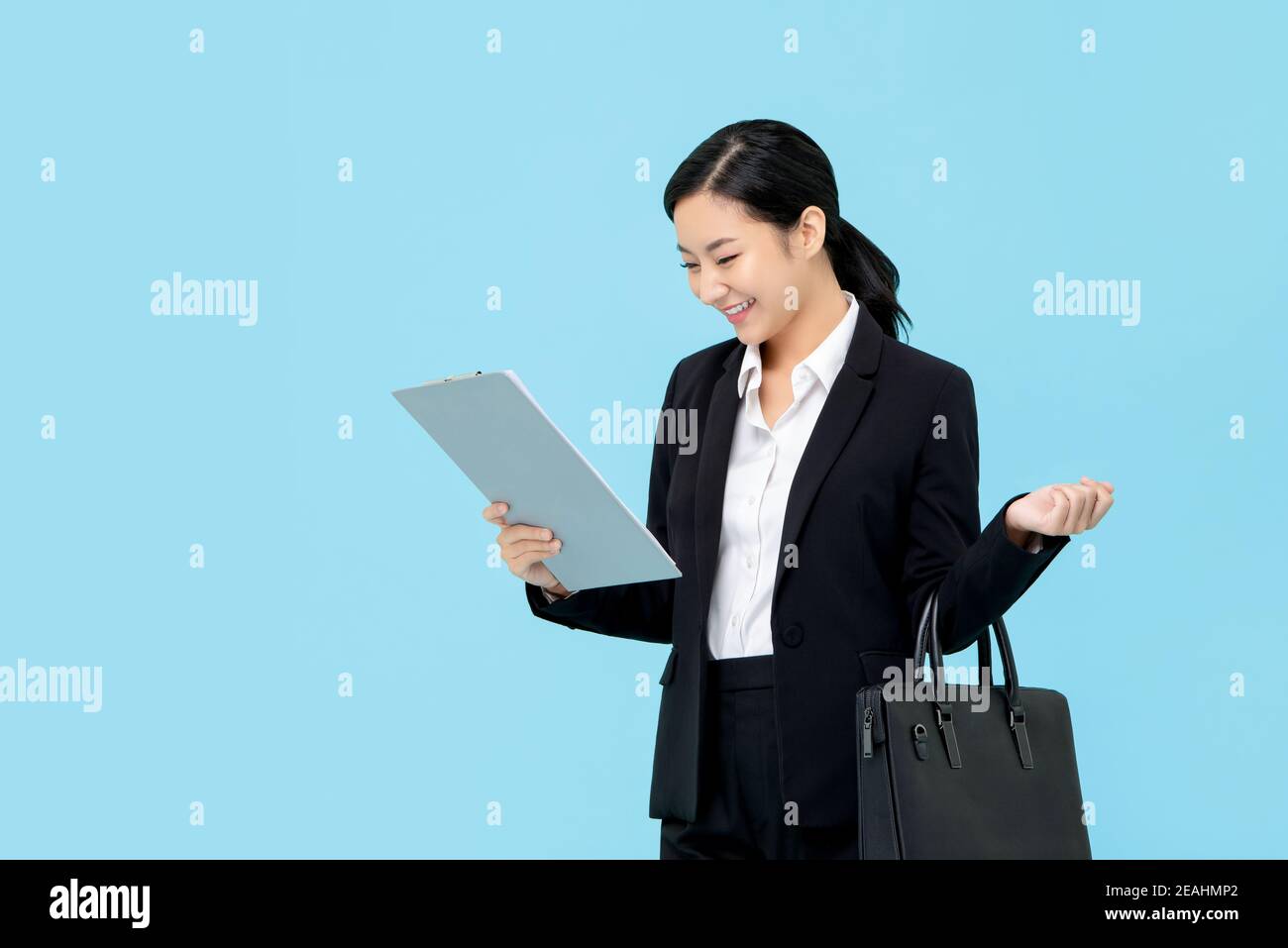 Professionelle asiatische Geschäftsfrau in formellen Anzug halten Aktentasche Blick auf Zwischenablage auf hellblauem Hintergrund isoliert Stockfoto