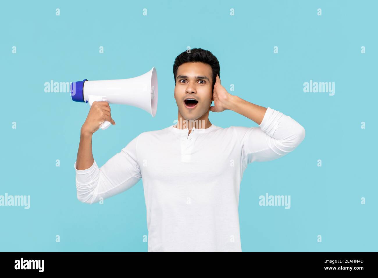 Überrascht asiatischen Mann hören Stimme auf Megaphon isoliert auf Hellblauer Hintergrund Stockfoto