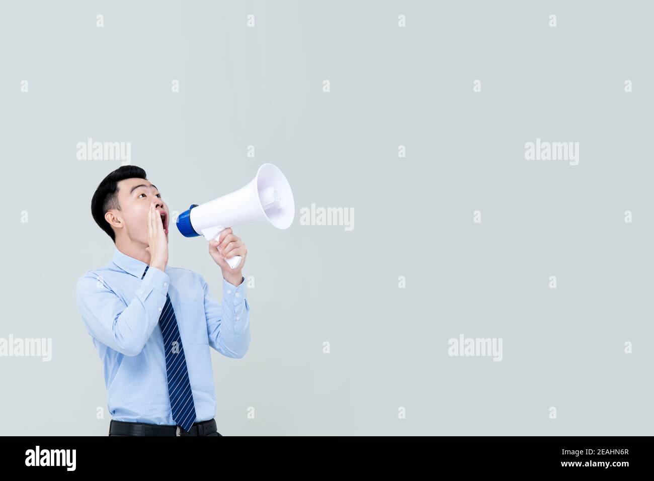 Asiatischer Mann im Geschäft Attrie schreiend auf Megaphon isoliert auf Hellgrauer Hintergrund mit Kopierbereich Stockfoto