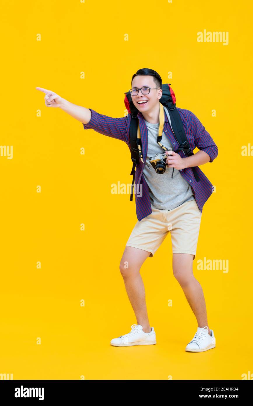 Junge gutaussehende glücklich asiatischen Mann in touristischen Kleidung mit Rucksack Und die Brille lächelt und zeigt, während die Kamera isoliert auf hält Gelber Hintergrund Stockfoto Junge gutaussehende glücklich asiatischen Mann in touristischen Kleidung mit Rucksack Und die Brille lächelt und zeigt, während die Kamera isoliert auf hält Gelber Hintergrund Stockfoto