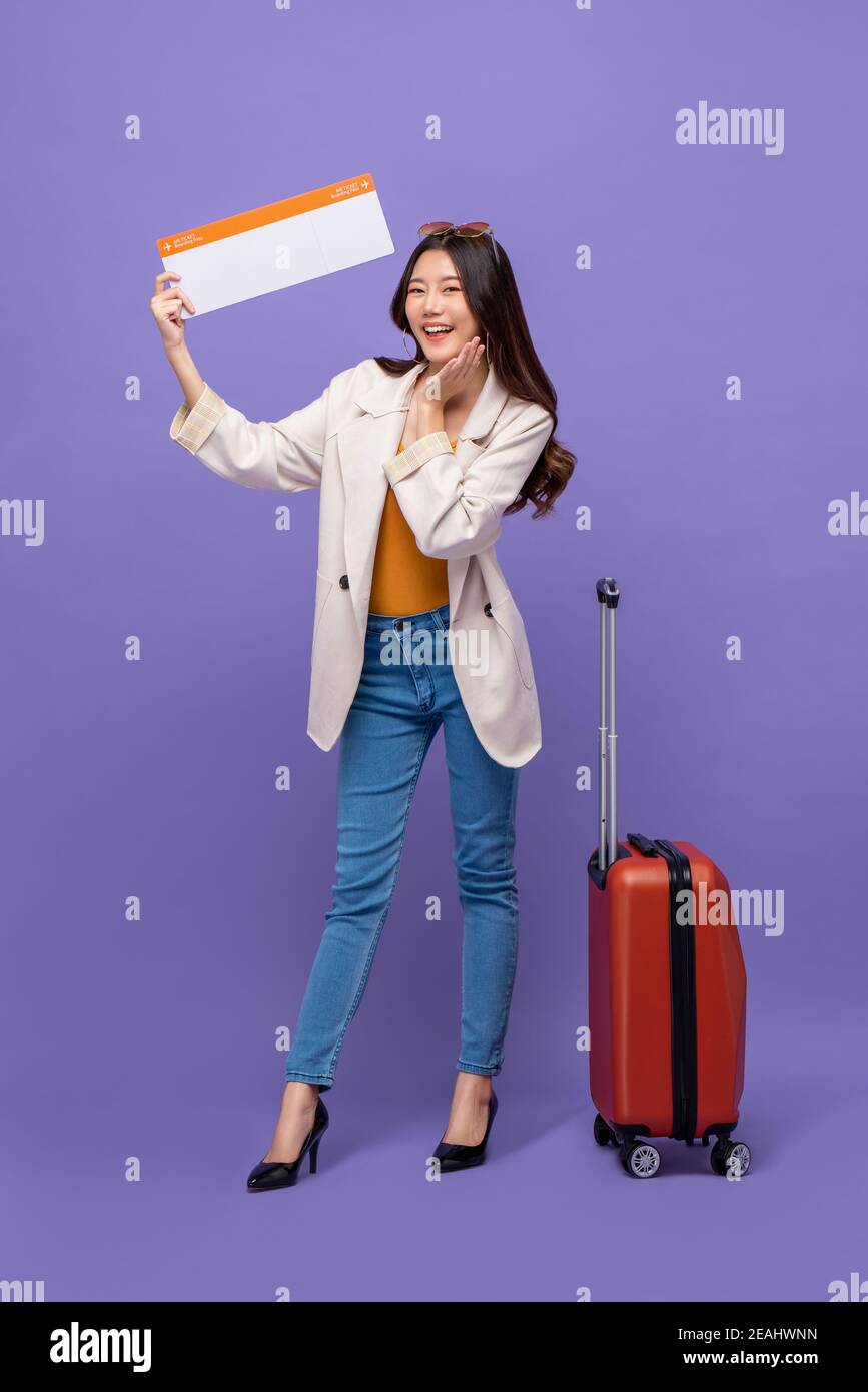Voller Körper von attraktiven jungen asiatischen Frau Tourist mit Gepäck Zeigt bestätigte Bordkarte isoliert auf violettem Studiohintergrund Stockfoto