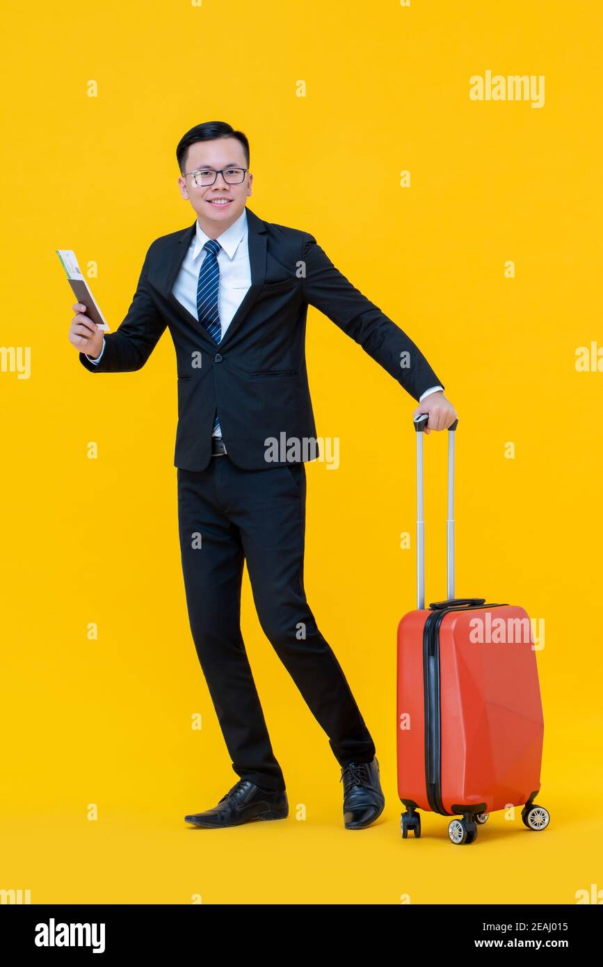 Lächelnder asiatischer Geschäftsmann mit Koffer, der Pass und Boarding hält Pass bereit für Reisen isoliert auf gelbem Hintergrund zu gehen Stockfoto Lächelnder asiatischer Geschäftsmann mit Koffer, der Pass und Boarding hält Pass bereit für Reisen isoliert auf gelbem Hintergrund zu gehen Stockfoto