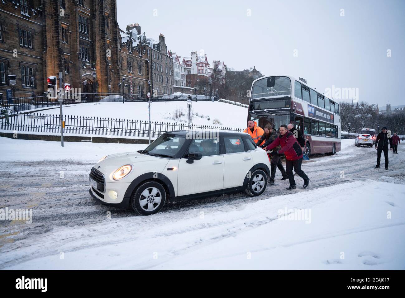 Edinburgh, Schottland, Großbritannien. Februar 2021, 10. In Großbritannien setzt sich der große Frost fort, und der schwere Schnee über Nacht und Morgen bringt den Verkehr auf vielen Straßen im Stadtzentrum zum Stillstand. PIC; Leute schieben Auto den Hügel hinauf, um den Weg für den Bus frei zu machen. Iain Masterton/Alamy Live Nachrichten Stockfoto