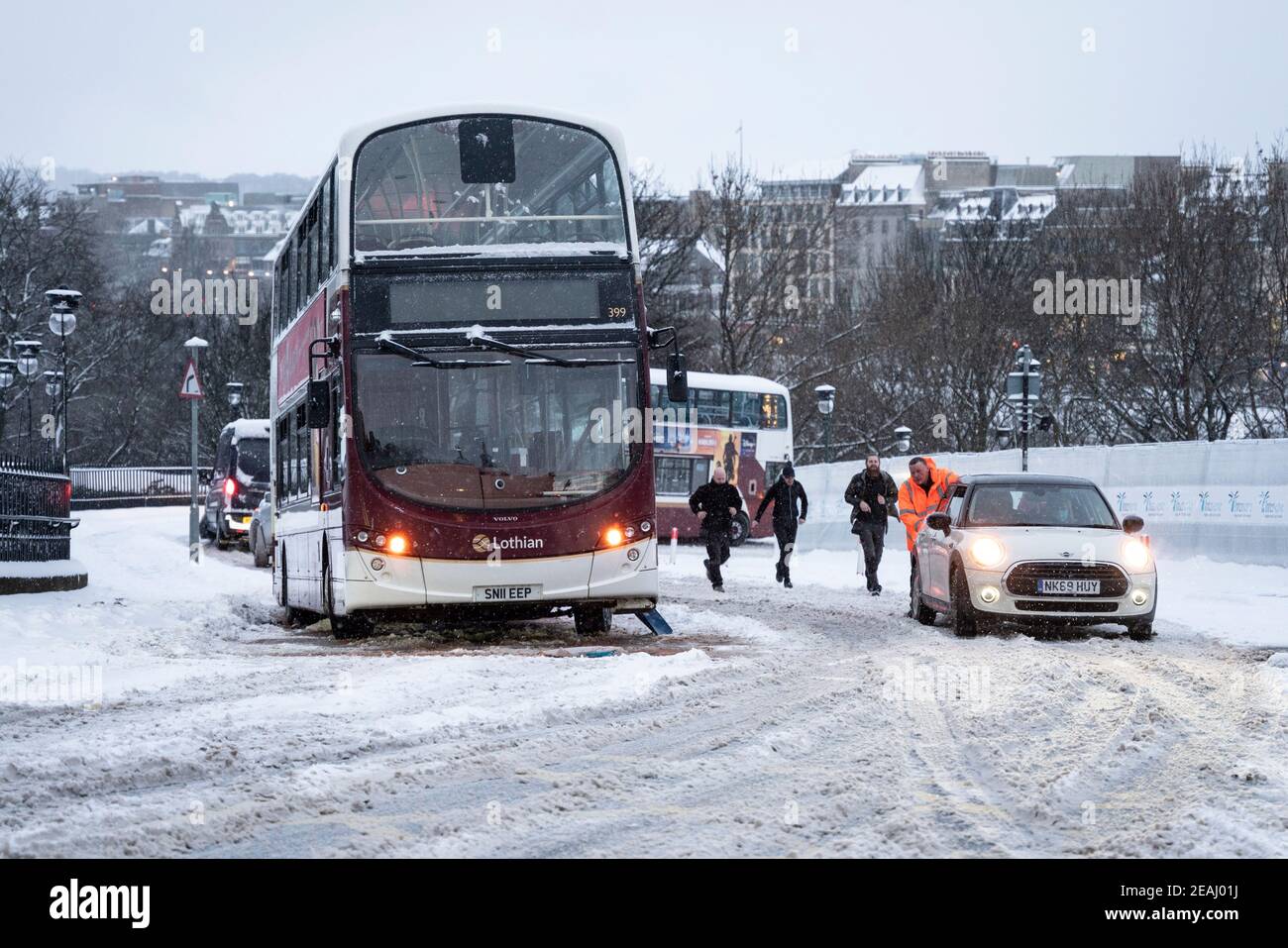 Edinburgh, Schottland, Großbritannien. Februar 2021, 10. In Großbritannien setzt sich der große Frost fort, und der schwere Schnee über Nacht und Morgen bringt den Verkehr auf vielen Straßen im Stadtzentrum zum Stillstand. PIC; Leute schieben Auto den Hügel hinauf, um den Weg für den Bus frei zu machen. Iain Masterton/Alamy Live Nachrichten Stockfoto