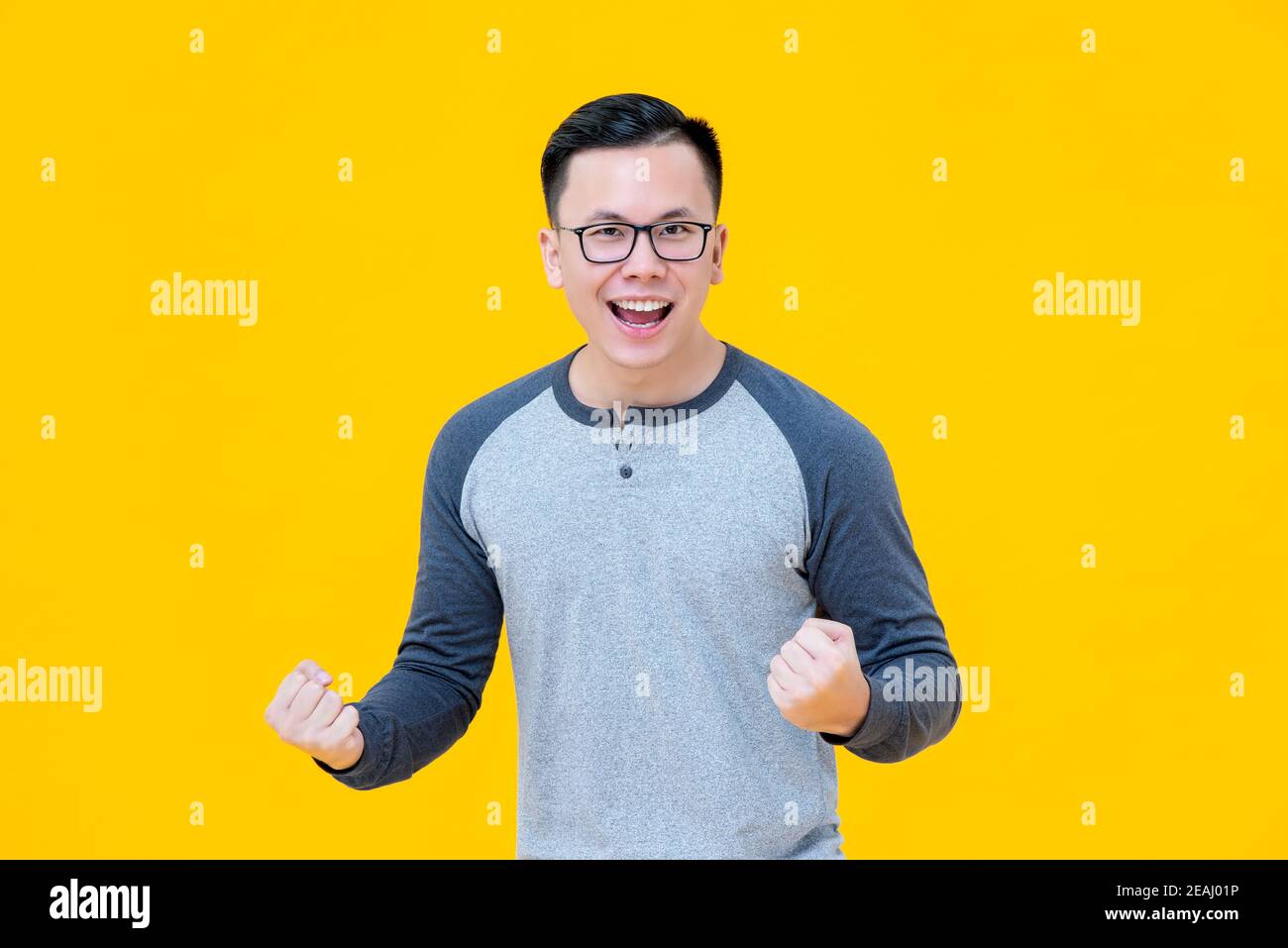 Portrait des begeisterten Siegers Asian Mann seine Fäuste mit Lächelndes Gesicht auf gelbem Hintergrund Stockfoto