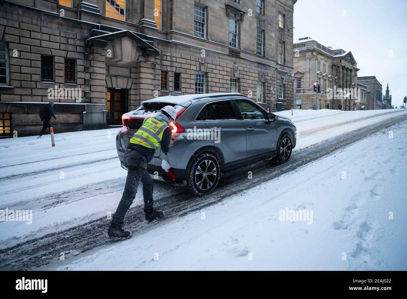 Edinburgh, Schottland, Großbritannien. Februar 2021, 10. In Großbritannien setzt sich der große Frost fort, und der schwere Schnee über Nacht und Morgen bringt den Verkehr auf vielen Straßen im Stadtzentrum zum Stillstand. PIC; der Mann schiebt das Auto auf den Hügel in der Altstadt. Iain Masterton/Alamy Live Nachrichten Stockfoto