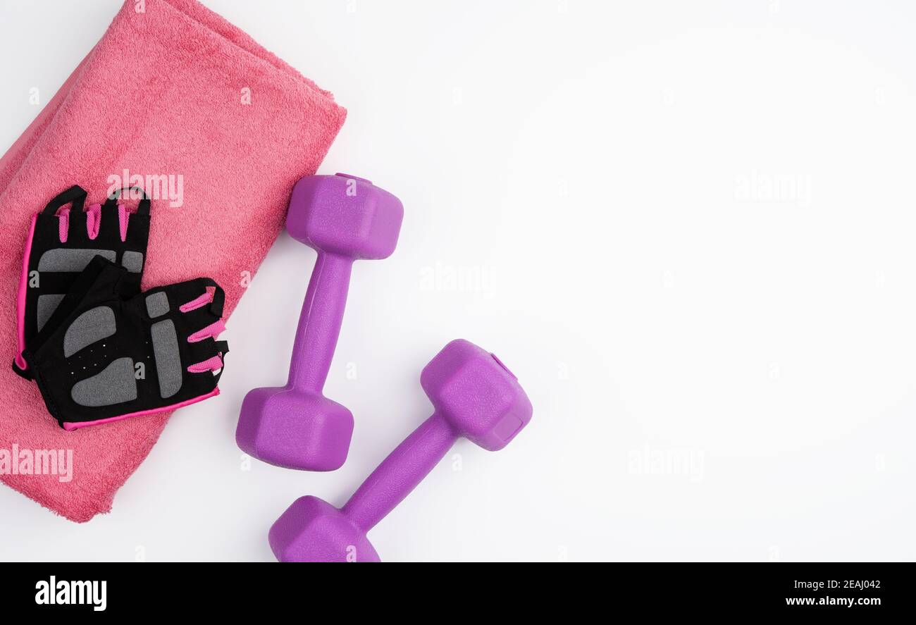 Handschuhe, ein Paar lila Hanteln und ein rosa Handtuch auf weißem Hintergrund Stockfoto