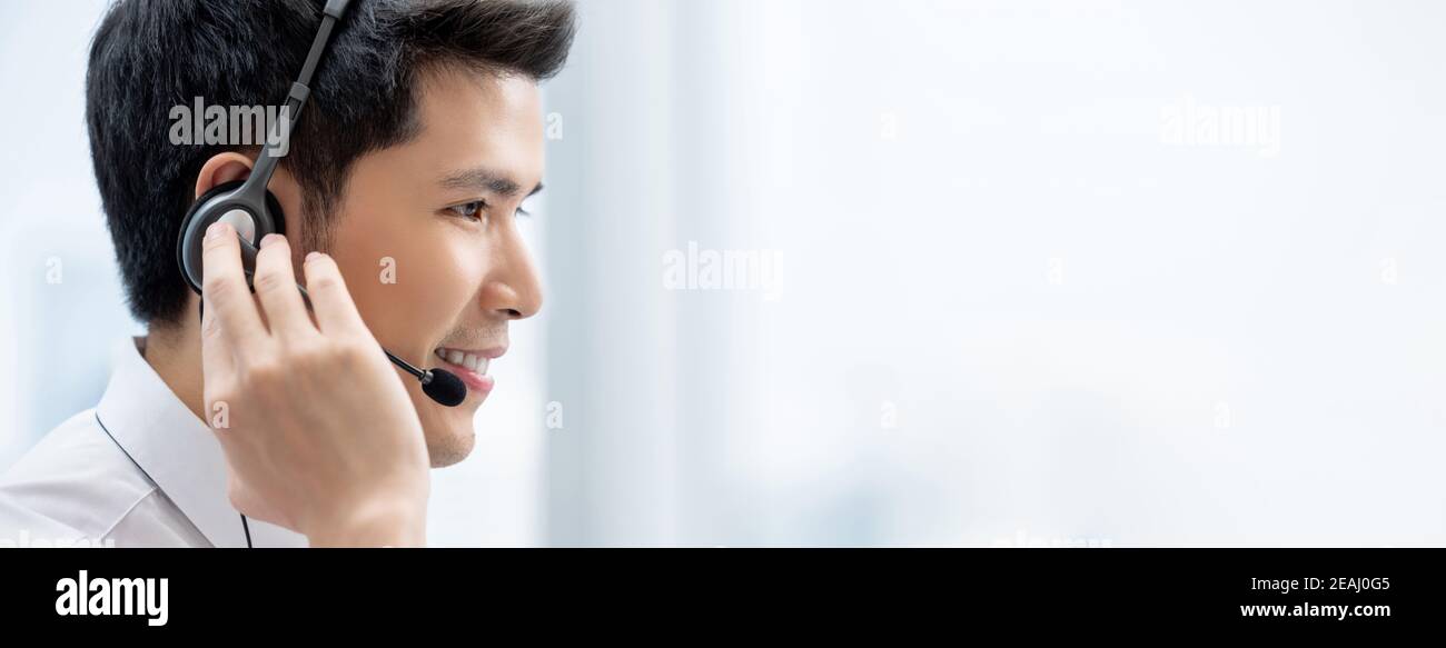 Lächelnder, hübscher asiatischer Mann mit Kopfhörern, der im Callcenter arbeitet Als Kundendienstbetreiber auf Bannerhintergrund mit Kopie Platz Stockfoto