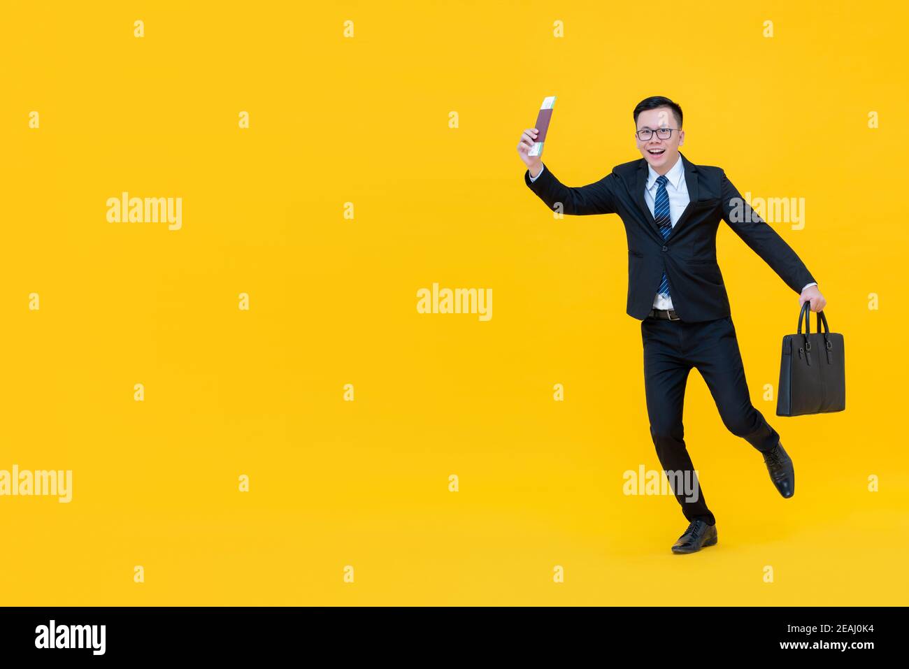 Junger asiatischer Mann im Business-Anzug mit Tasche, die Pass zeigt Und die Bordkarte, die für die Reise auf gelb gehen soll Hintergrund mit Kopierbereich Stockfoto