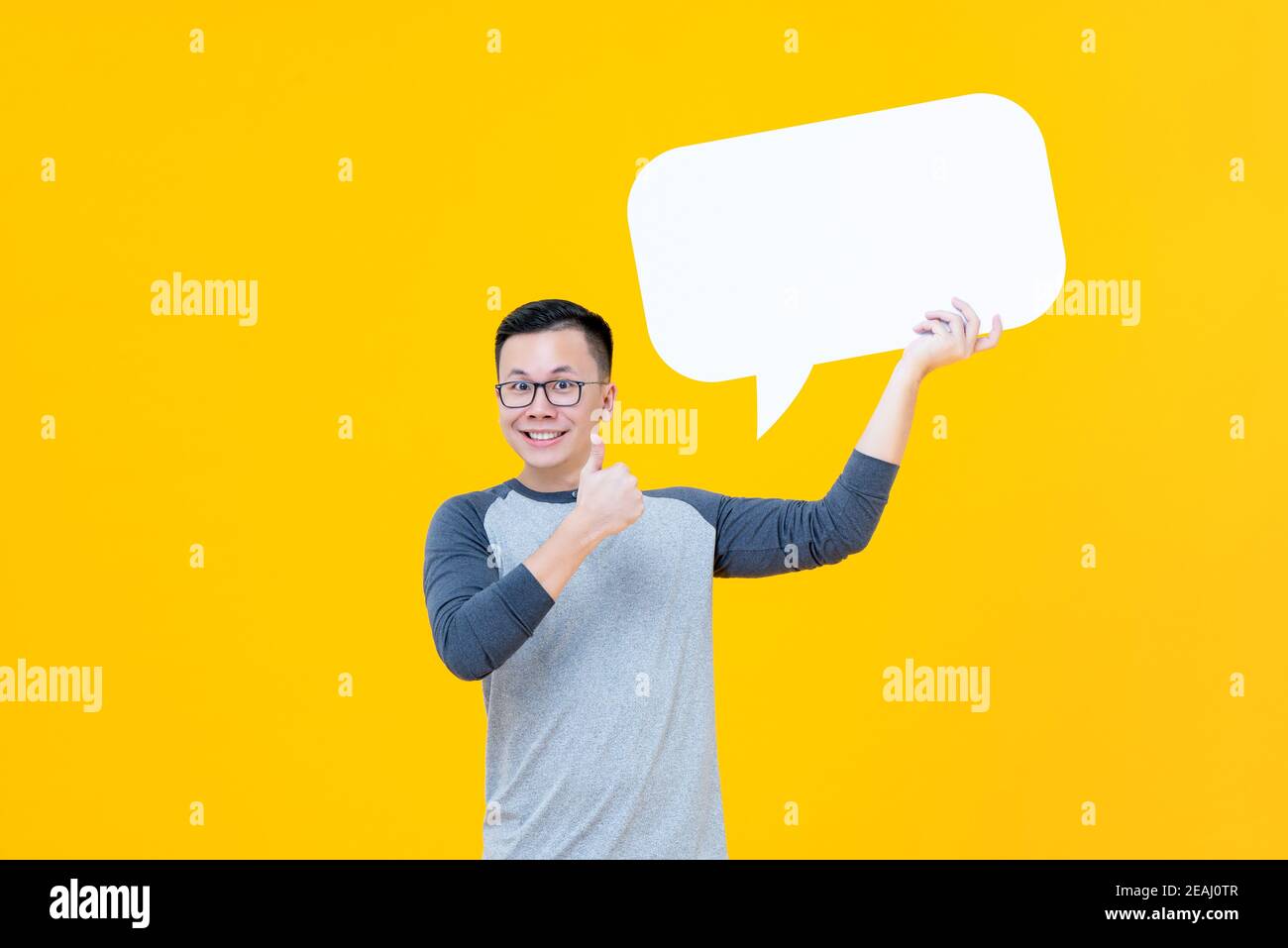 Lächelnder asiatischer Mann, der der leeren Sprechblase Daumen hoch gibt Mit Platz für Text auf gelbem Hintergrund isoliert Stockfoto