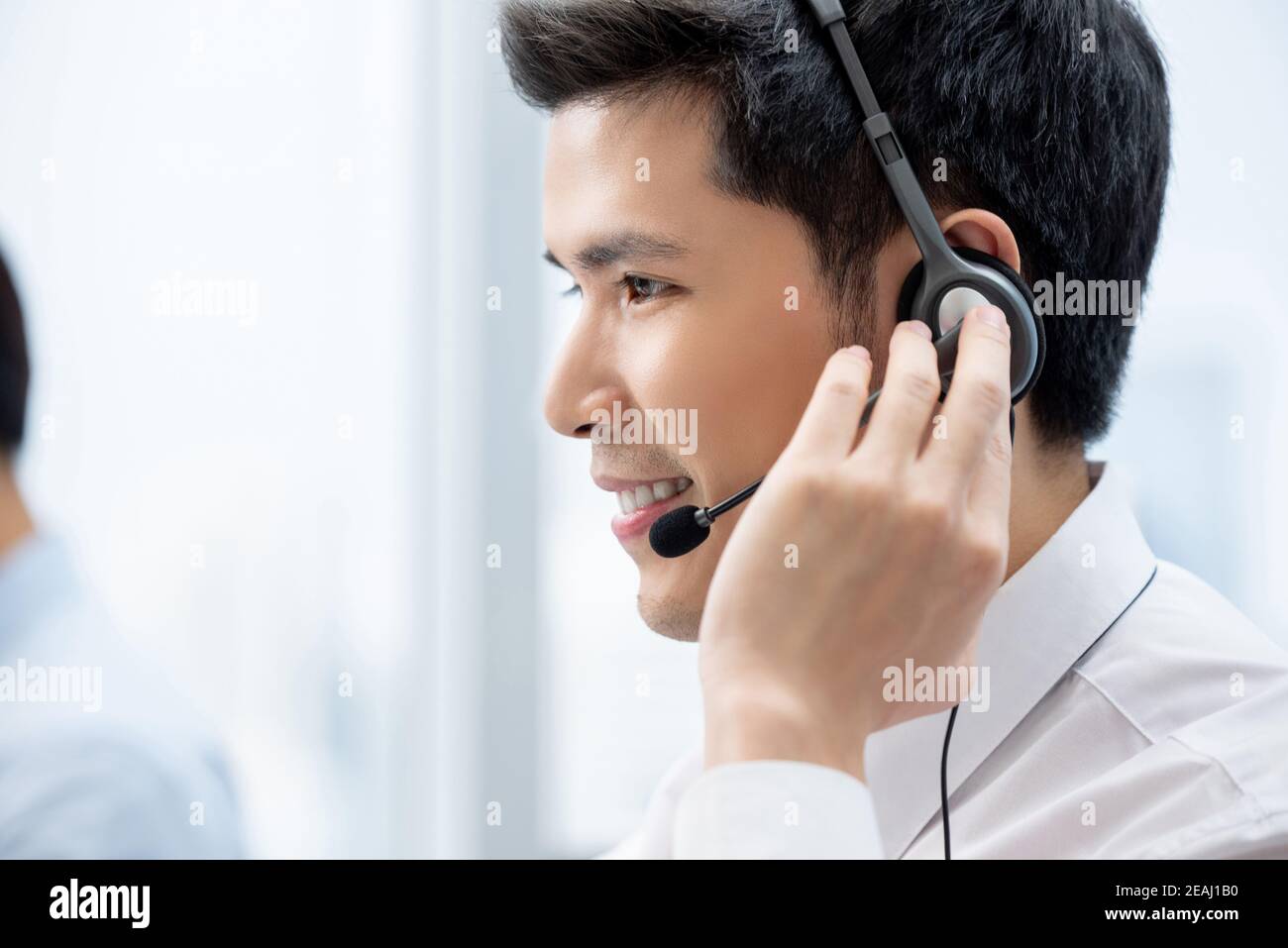 Lächelnd gut aussehende asiatische Mann arbeitet im Call Center Büro als Ein Kundendienstbetreiber Stockfoto