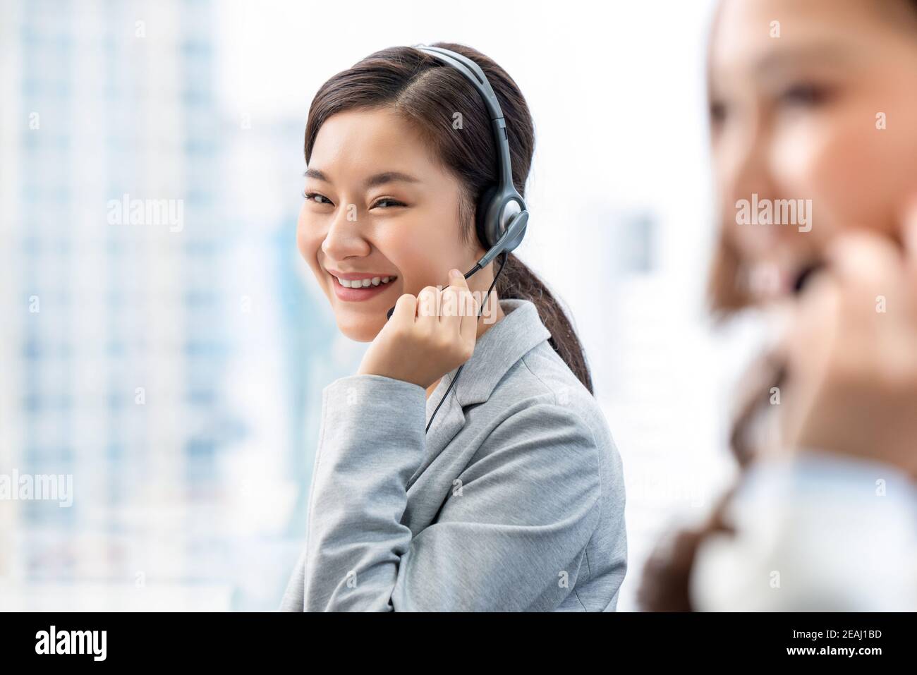 Lächelnde, schöne Asianerin, die als Kundendienst-Bedienerin im Callcenter-Büro arbeitet Stockfoto
