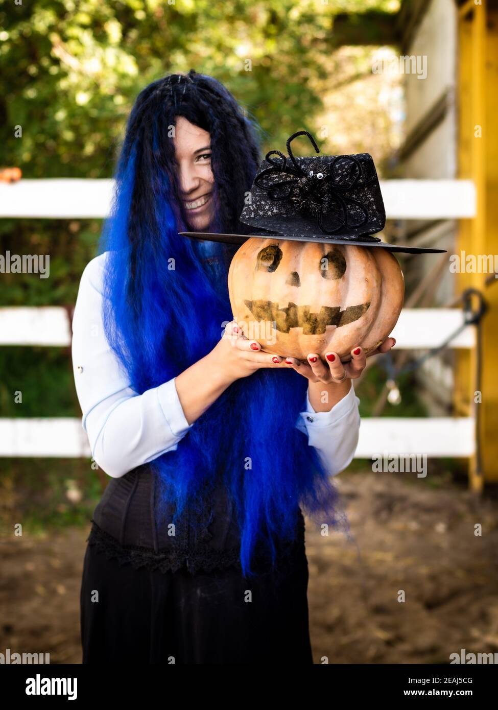 Ein Mädchen als Hexe mit blauen Haaren gekleidet ist Halten Sie einen Kürbis mit einem bemalten Gesicht und einer Hexe Kap Stockfoto