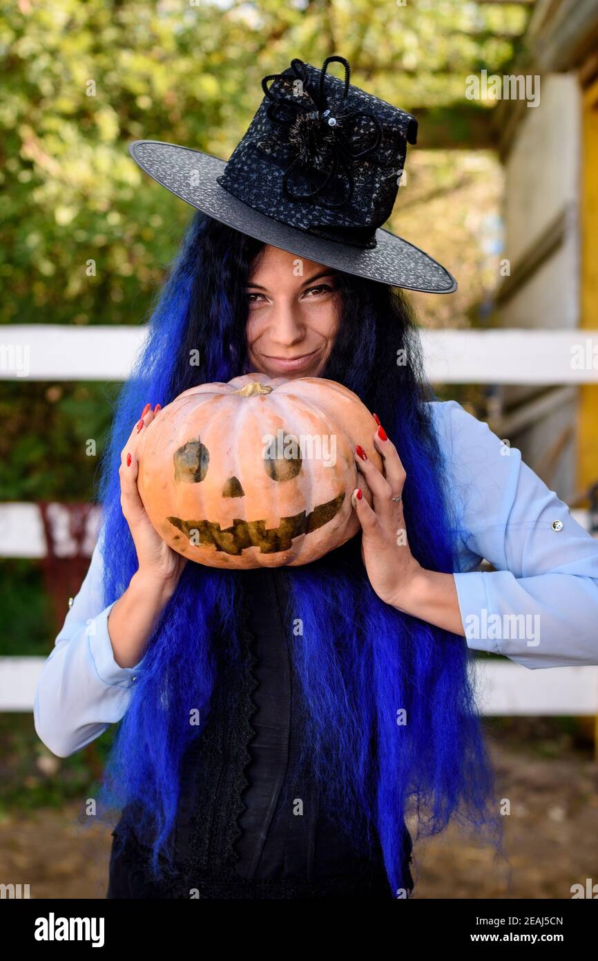 Ein Mädchen in einem Hexenkostüm mit blauen Haaren ist Halten Sie einen Kürbis mit einem bemalten Gesicht Stockfoto