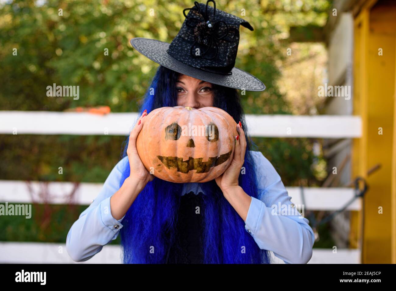 Ein Mädchen in einem Hexenkostüm schaut von hinten heraus Ein Kürbis mit einem bemalten Gesicht Stockfoto