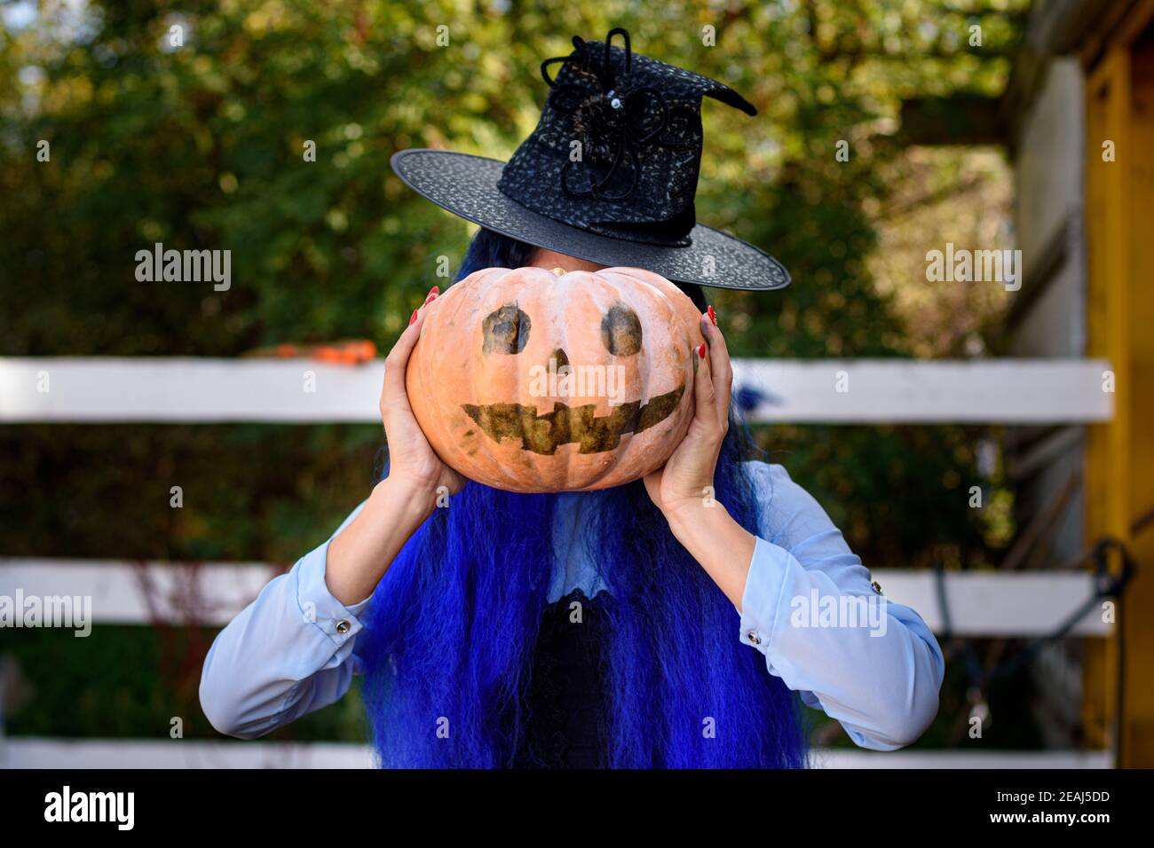 Ein Mädchen, das als Hexe gekleidet war, bedeckte ihr Gesicht mit Ein Kürbis mit einem bösen Gesicht im Stil gezeichnet Einer Halloween-Feier Stockfoto