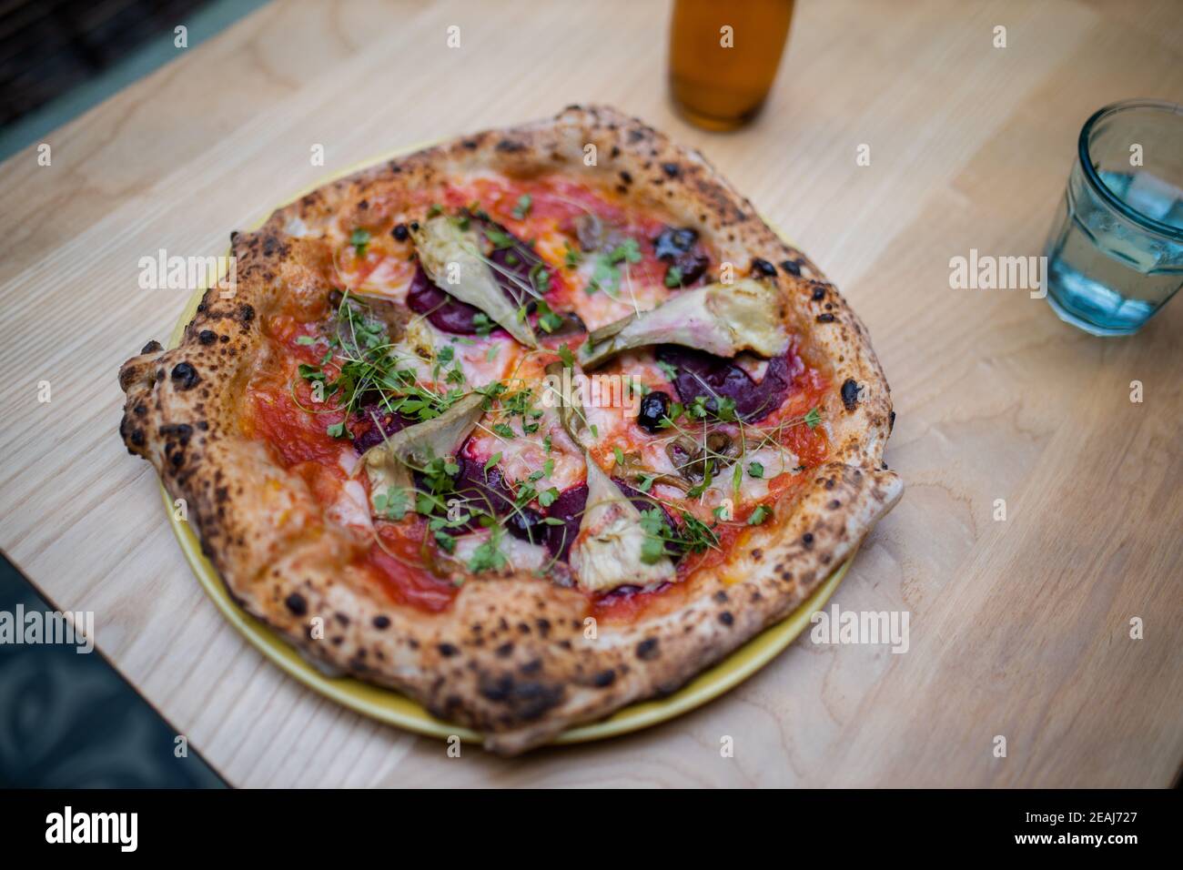 Vegane Pizza auf einem Tisch neben einer Flasche Dressing Und ein Glas Wasser Stockfoto