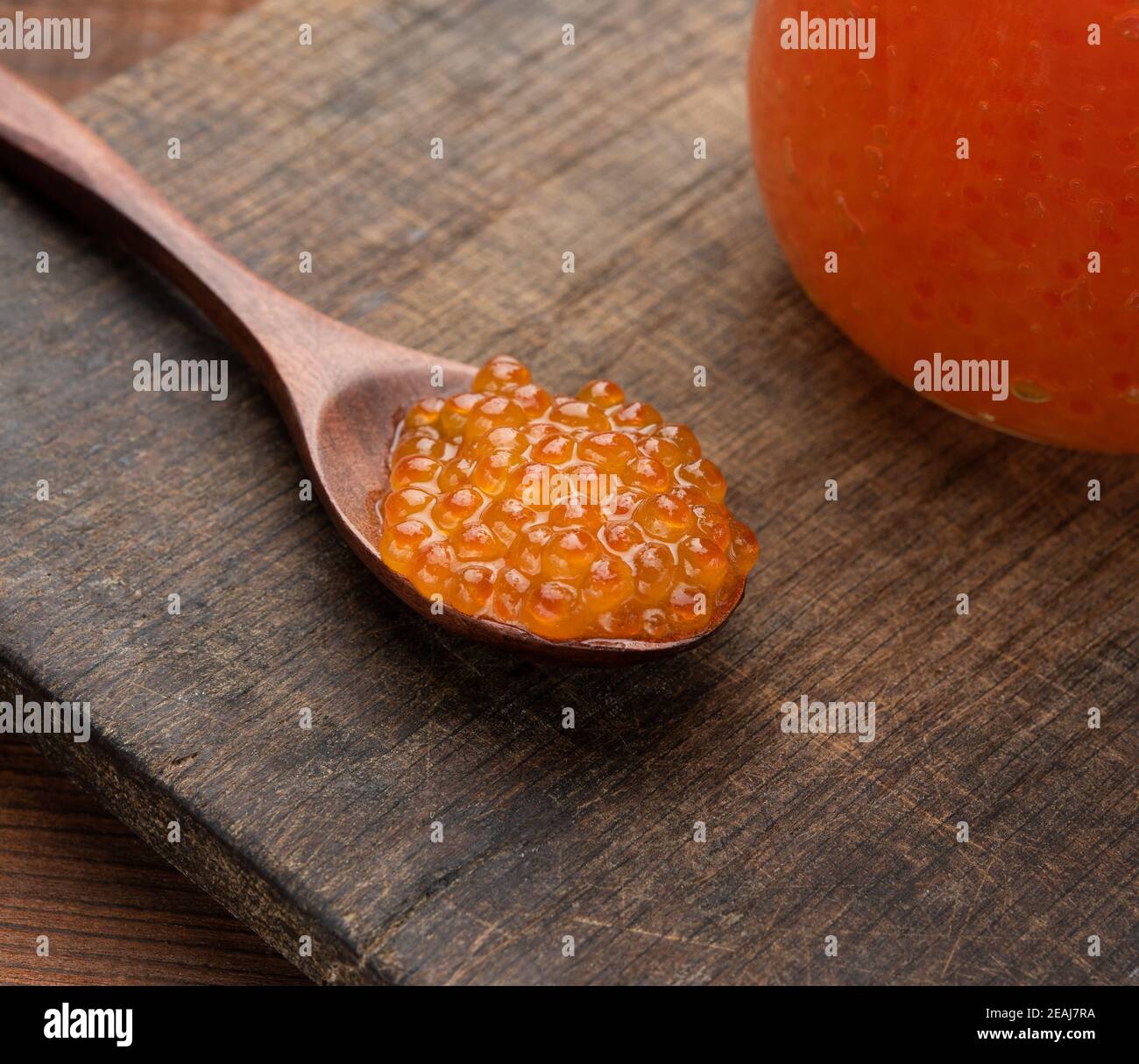 Roter Kaviar in einem braunen Holzlöffel auf dem Tisch, hinter einem vollen Glas Kaviar Stockfoto Roter Kaviar in einem braunen Holzlöffel auf dem Tisch, hinter einem vollen Glas Kaviar Stockfoto
