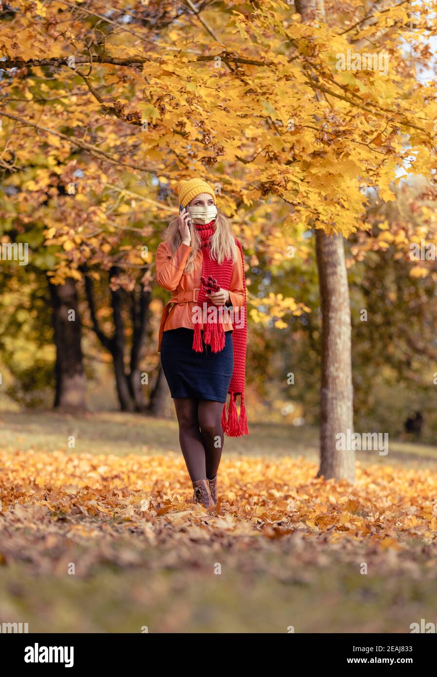 Frau mit ihrem Telefon zu Fuß in Herbst Park während Coronavirus-Krise Stockfoto