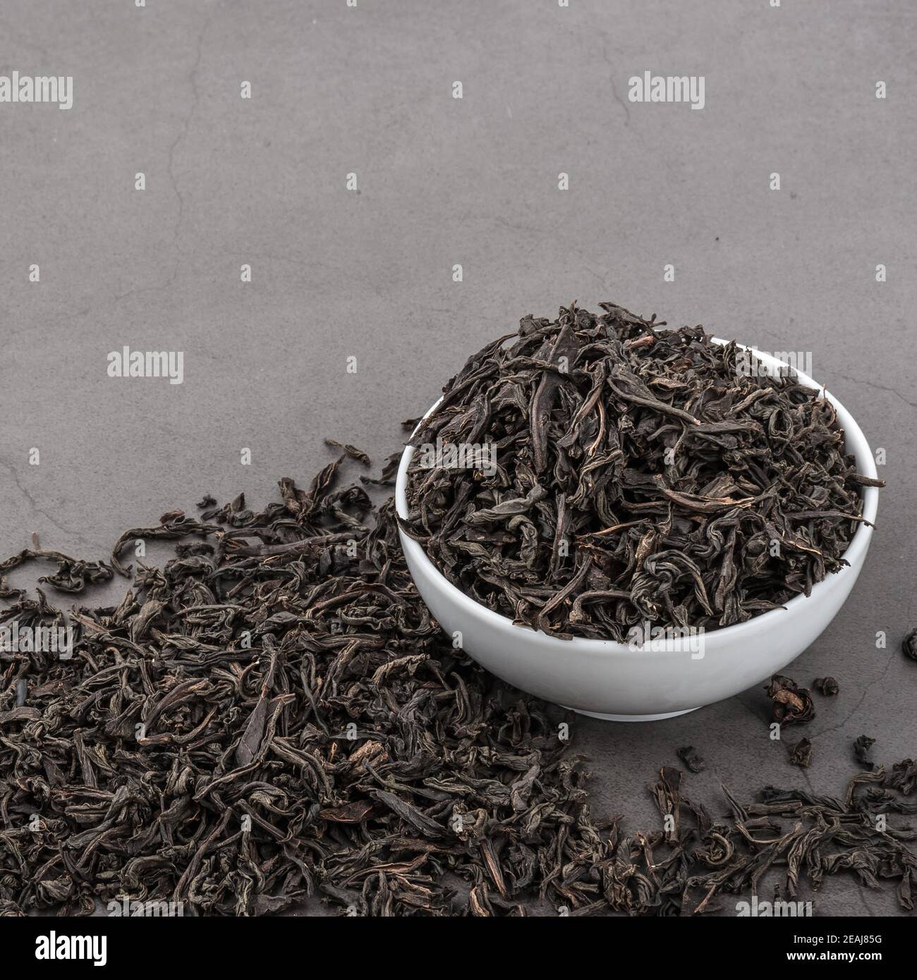 Getrockneter Tee wird in eine weiße Keramikschale auf einem grauen strukturierten Hintergrund gegossen. Stockfoto