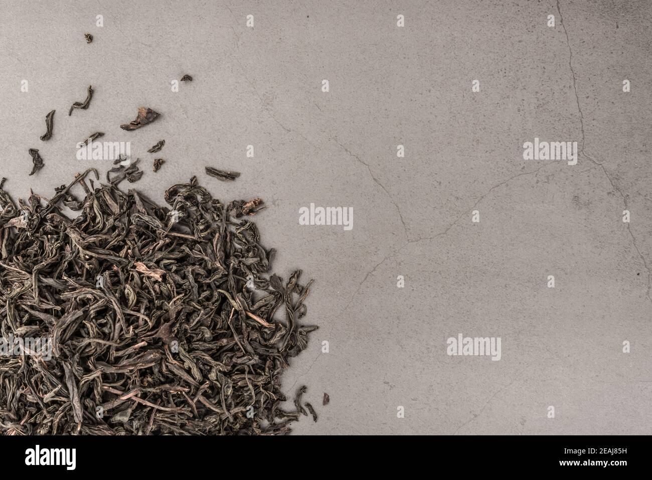 Getrockneter Tee wird auf einem grauen strukturierten Hintergrund gestreut gegossen. Stockfoto