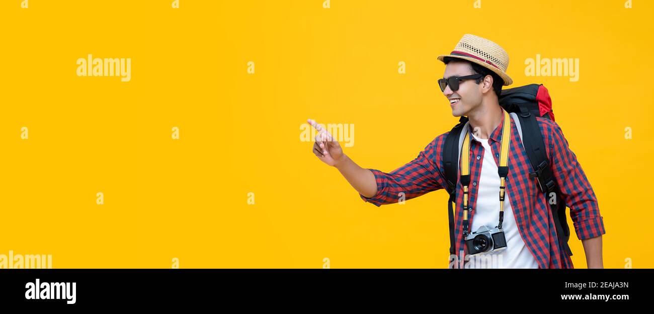 Fröhlich gut aussehenden indischen Mann Tourist mit Kamera und Rucksack tragen hut und Sonnenbrille zeigen die Hand, um Platz gegen Gelb zu kopieren Hintergrund des Banners Stockfoto Fröhlich gut aussehenden indischen Mann Tourist mit Kamera und Rucksack tragen hut und Sonnenbrille zeigen die Hand, um Platz gegen Gelb zu kopieren Hintergrund des Banners Stockfoto