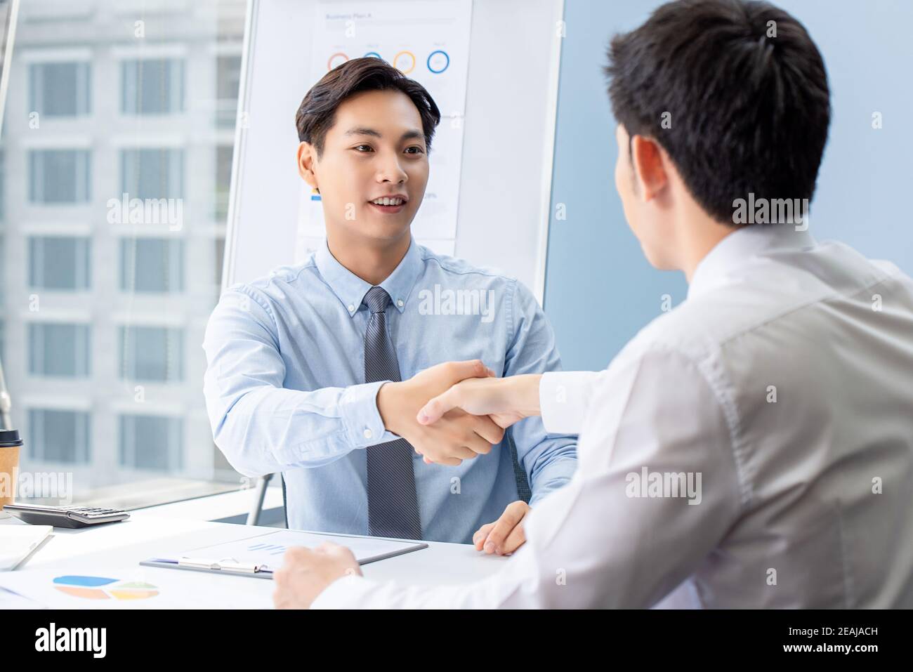 Junger asiatischer Geschäftsmann macht Handschlag mit Partner bei der Sitzung In Büros Stockfoto