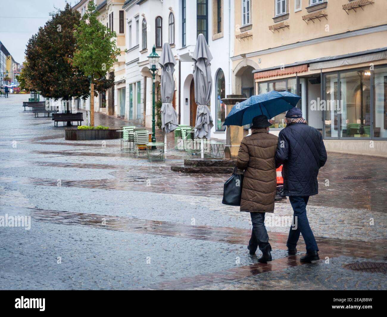 Ein paar ältere Leute, die im Regen in der Stadt spazieren gehen Stockfoto