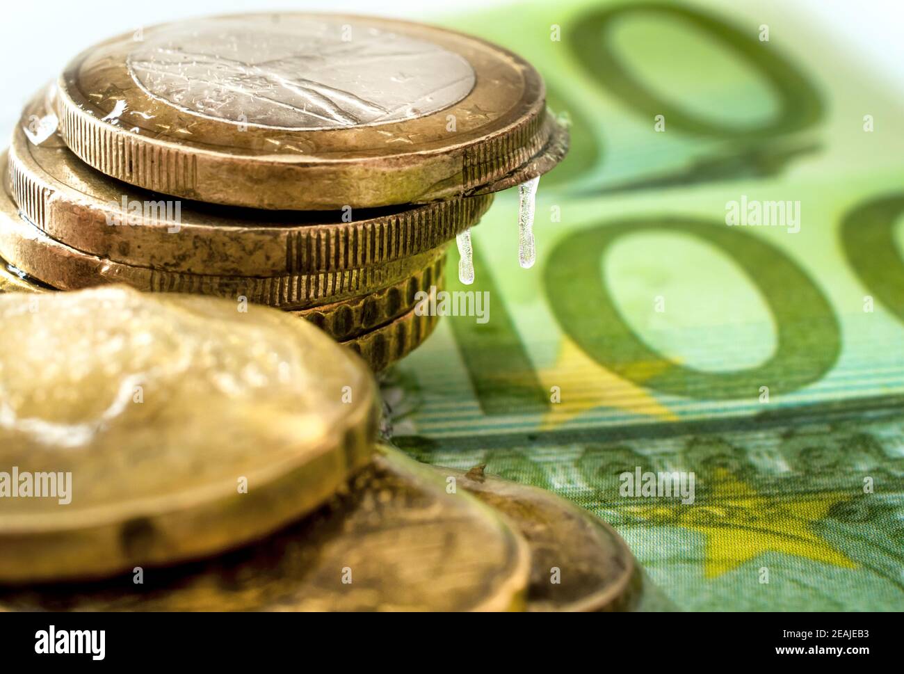 100-Euro-Banknote und im Eis eingefrorene Euro-Münzen. Gefrorenes Geld, Euro im Eis mit Eiszapfen Stockfoto