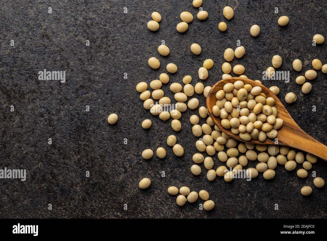 Getrocknete Sojabohnen in Holzlöffel auf schwarzem Tisch. Stockfoto