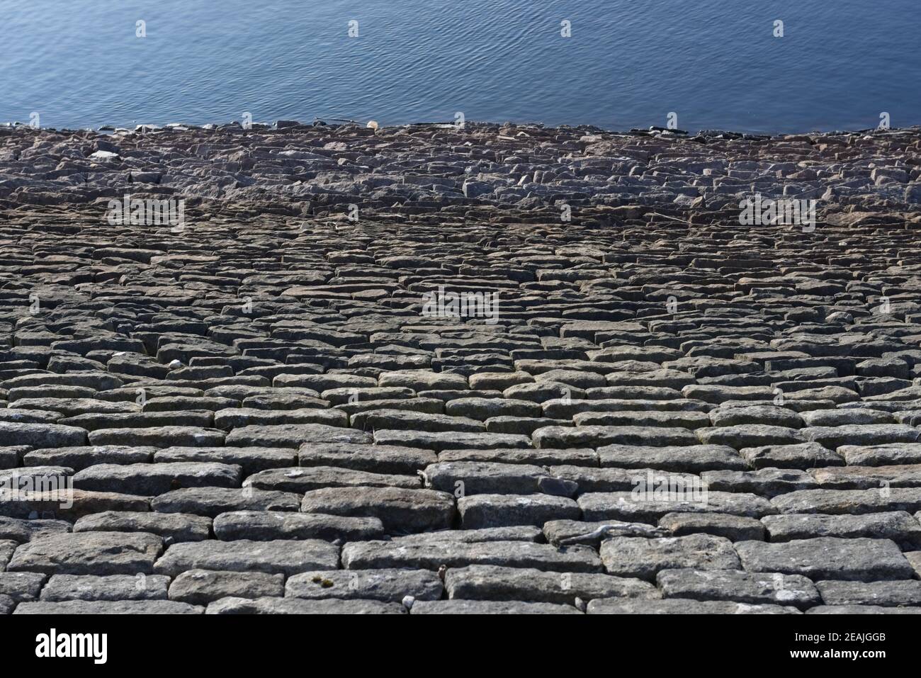 Abstrakte Staumauer, Blick hinunter auf tiefblaues Wasser, sonnige Steine Stockfoto