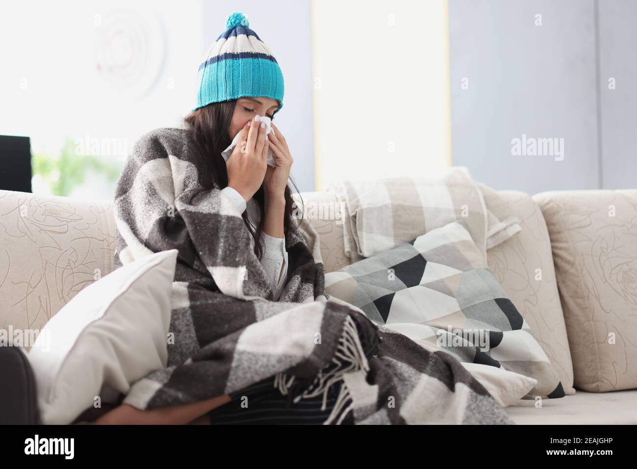 Gekühlte Frau auf Sofa in Decke und Hut hält Taschentuch Stockfoto Gekühlte Frau auf Sofa in Decke und Hut hält Taschentuch Stockfoto