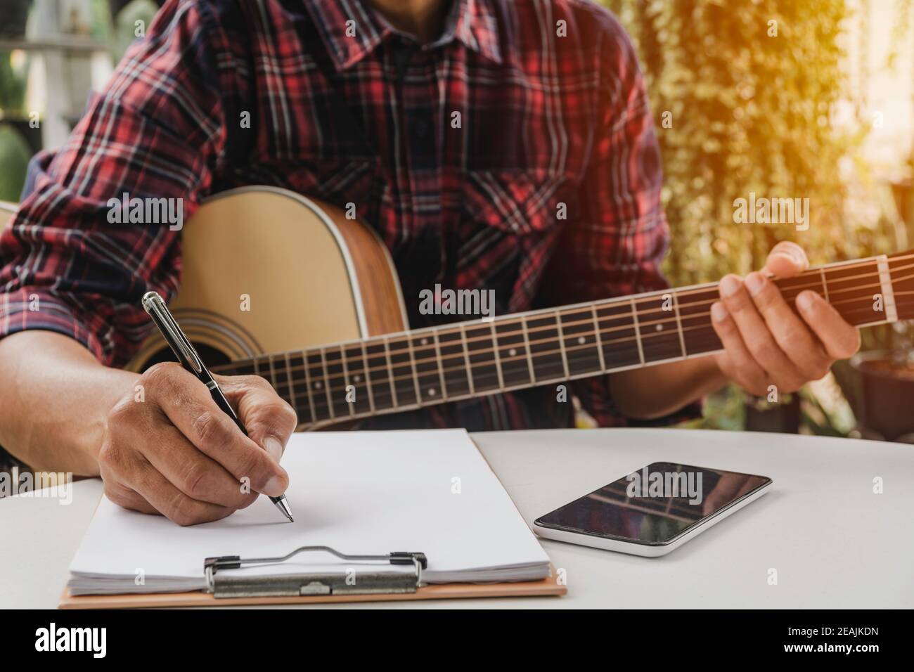 Ein Songwriter hält Stift für ein Lied zu komponieren. Musiker spielt akustische Gitarre. Live-Musik und abstraktes musikalisches Konzept. Stockfoto