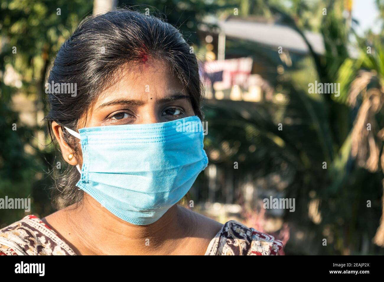 Lächelndes Gesicht mit Maske. Lächelnde Frau mit Gesichtsmaske. Nahaufnahme Vorderansicht einer glücklichen indischen Frau, die eine Gesichtsmaske trägt und lächelt und die Kamera anschaut. Gesundheitswesen Medizin Hintergrund Indien. Stockfoto