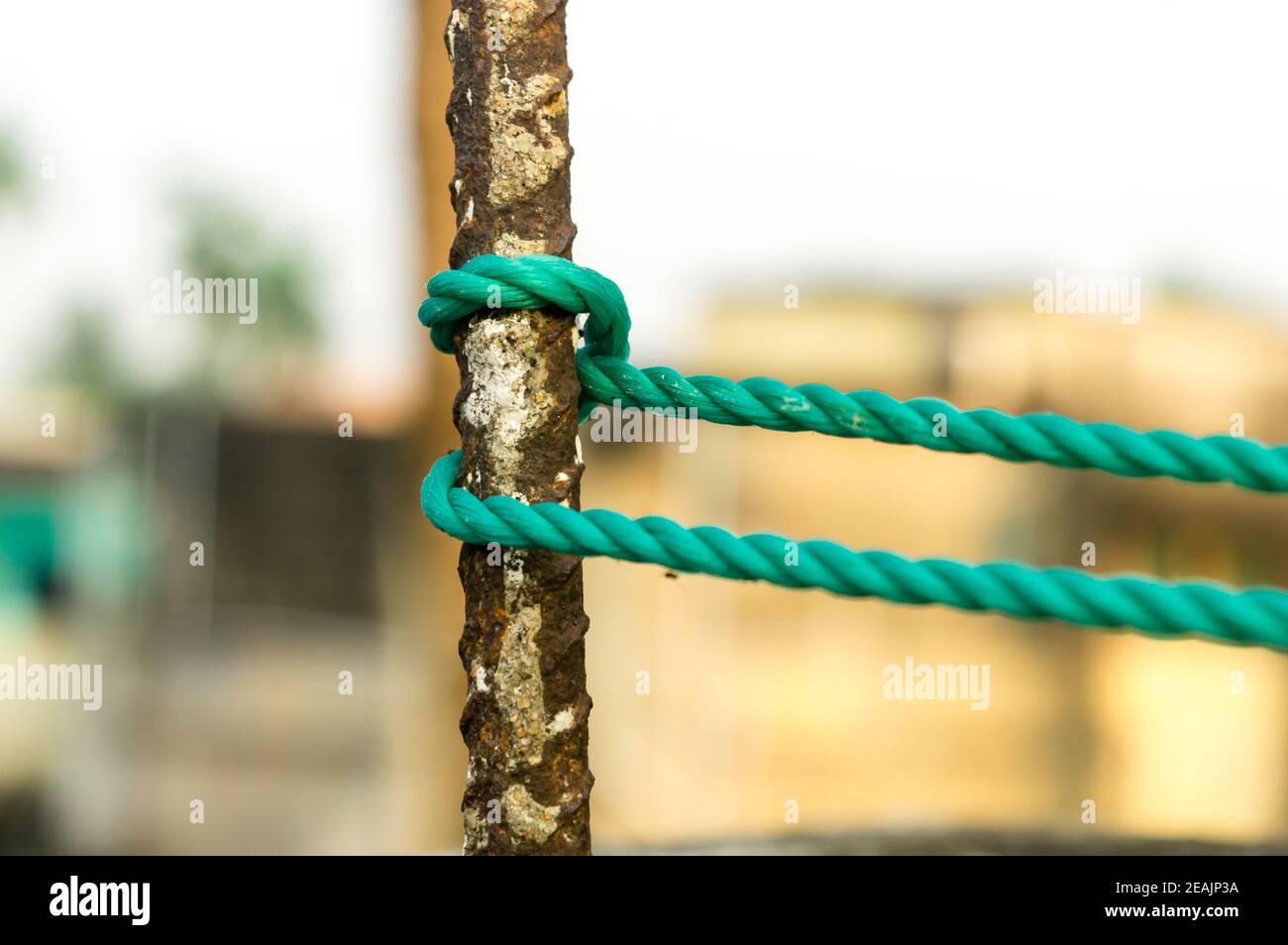 Ein Seil wird in einem Knoten um einen Zaunpfosten gebunden, Seil gebunden Hitch Knoten auf einem rostigen Eisenpol isoliert vom Hintergrund. Stockfoto