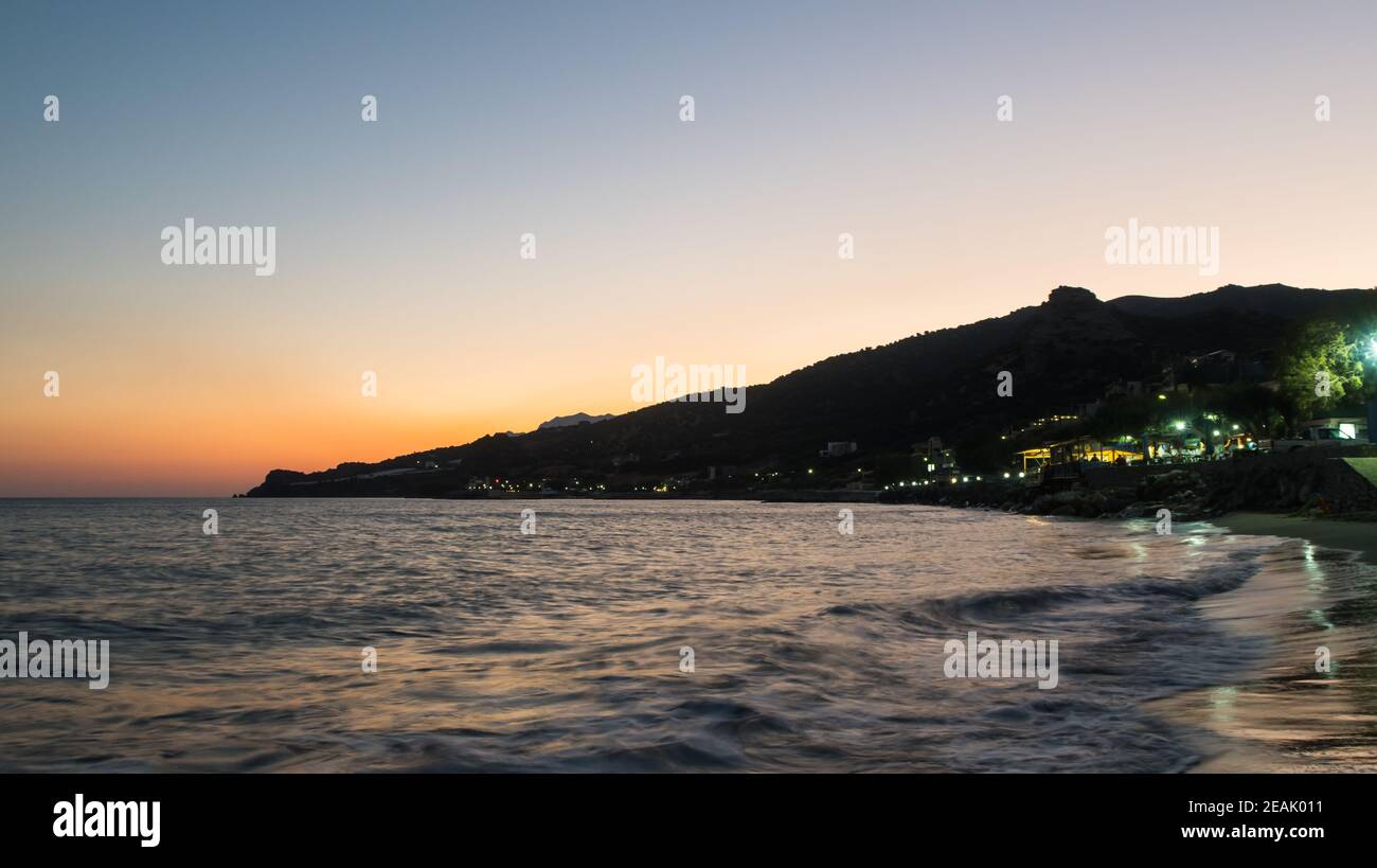 Seeufer bei Sonnenuntergang mit Bergen dahinter und wenig Wellen Stockfoto