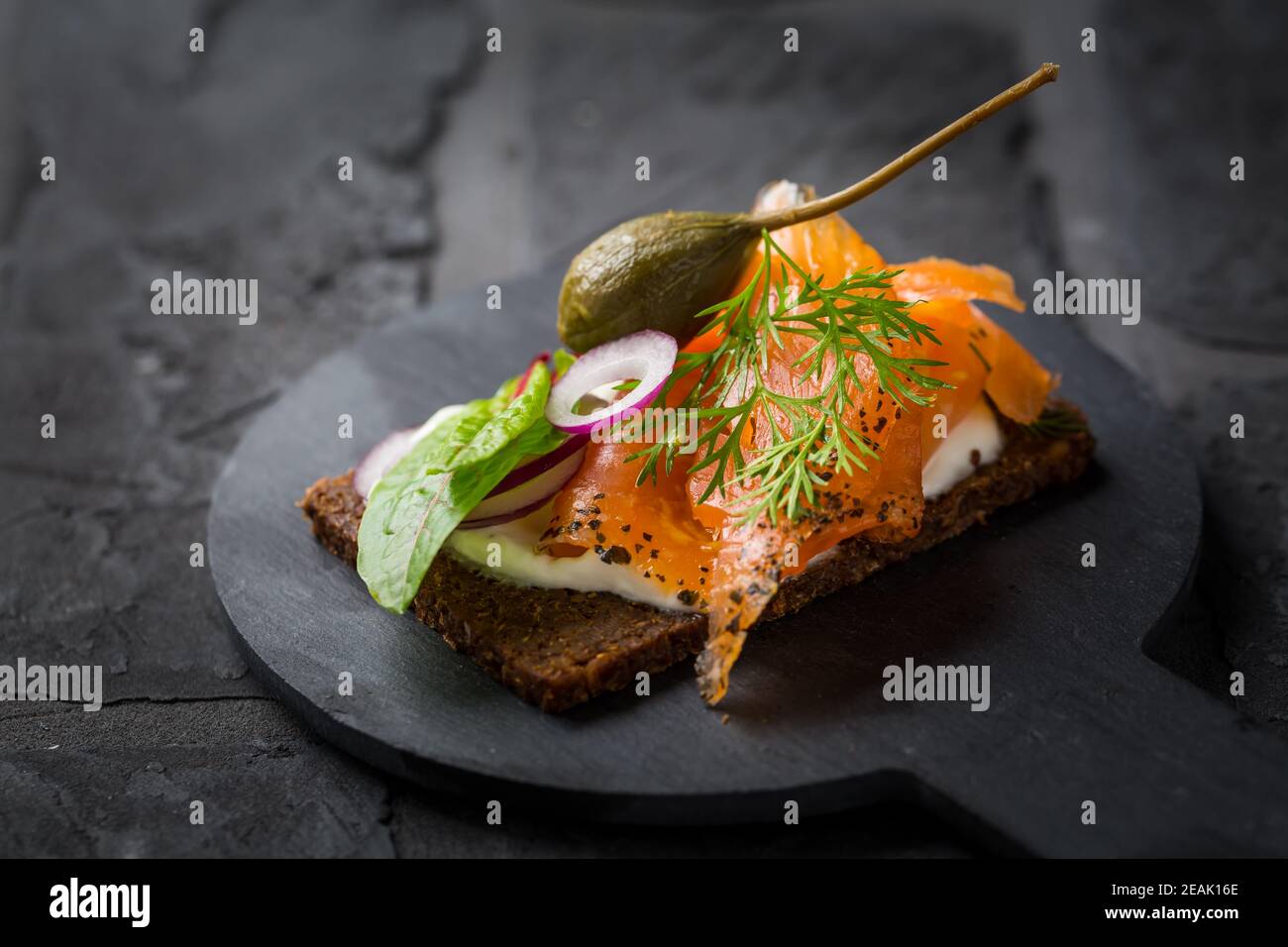 Lachs offenes Sandwich auf Pumpernickelbrot mit Gemüse, Kräutern und Weichkäse Stockfoto