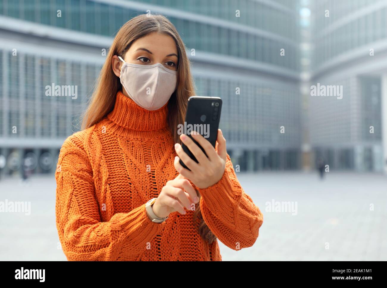 Junge Frau trägt Gesichtsmaske mit Smartphone-App in der modernen Stadt Straße. Speicherplatz kopieren. Stockfoto